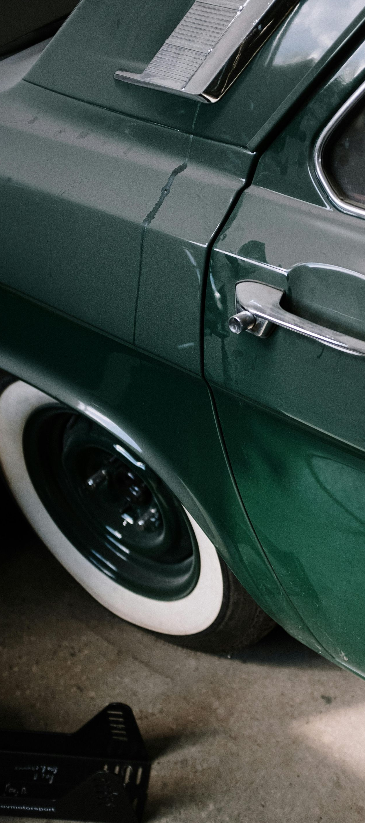 Green vintage car side with white-walled tires, chrome door handle, and trim.