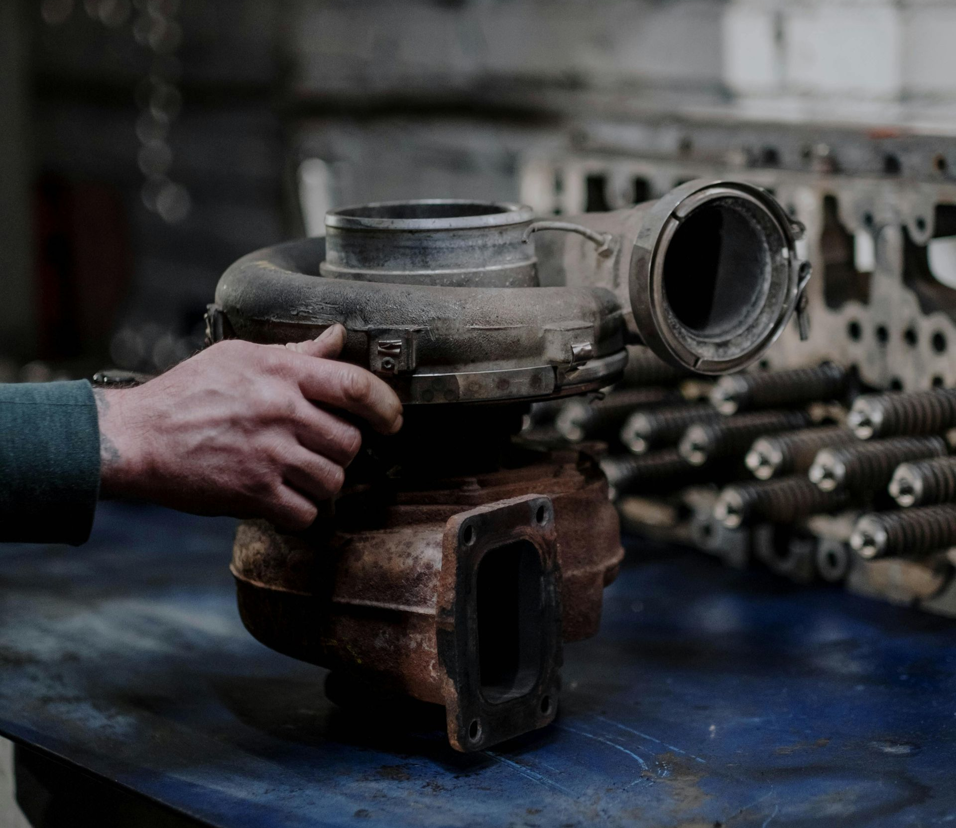 Person's hand holding a worn turbocharger, likely for a vehicle repair, in a workshop setting.