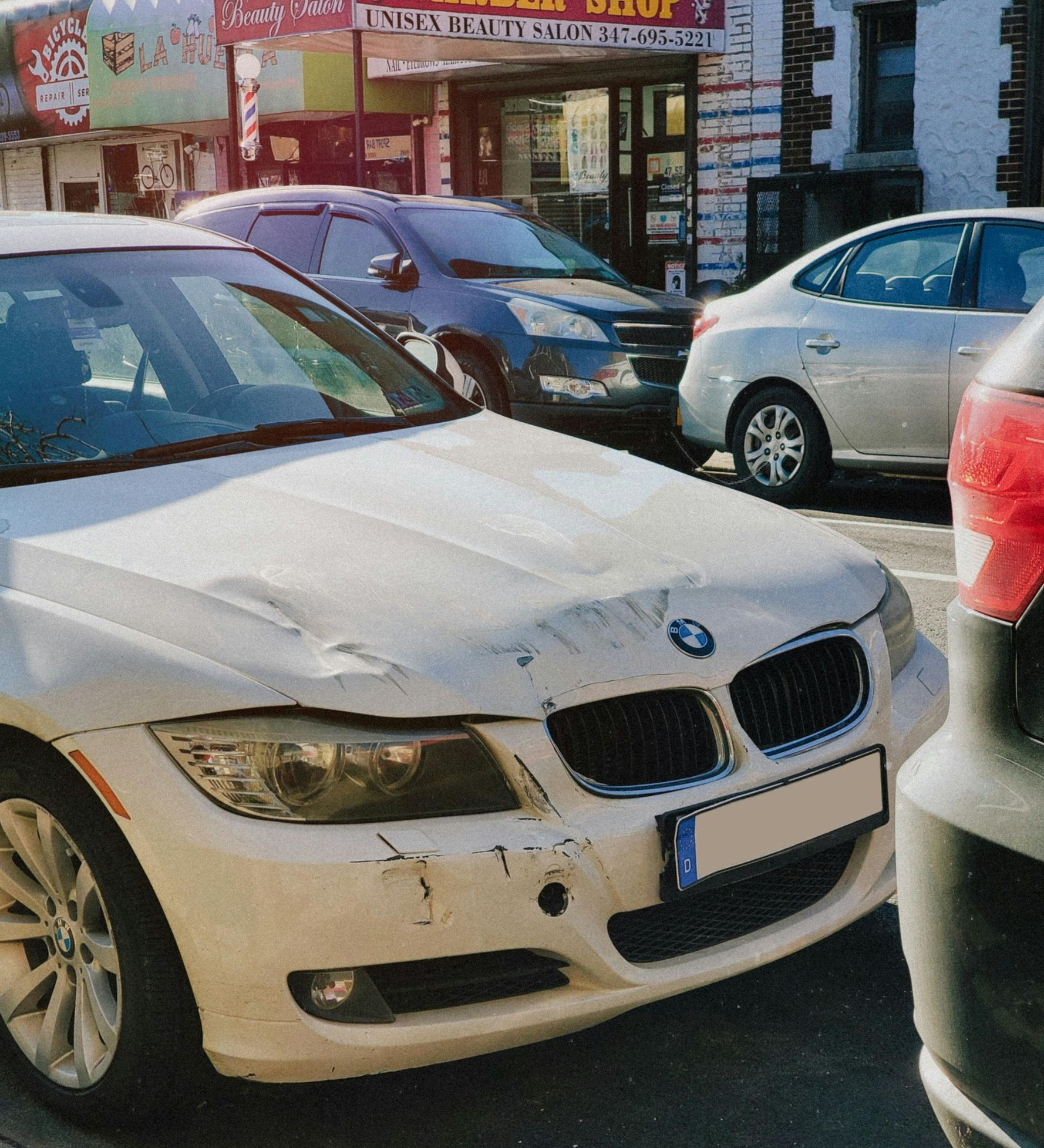 A damaged white BMW parked on a city street with other vehicles nearby.
