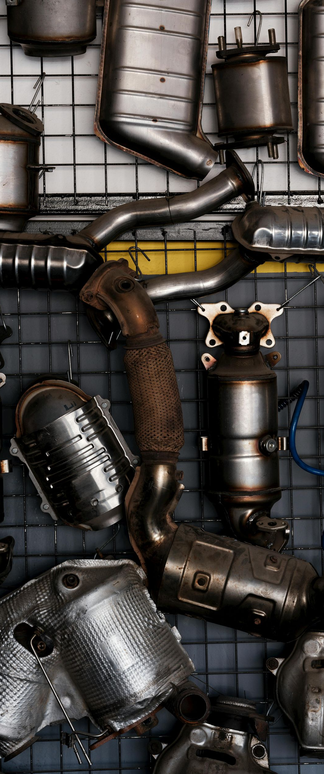 Various car catalytic converters hanging on a wire grid.