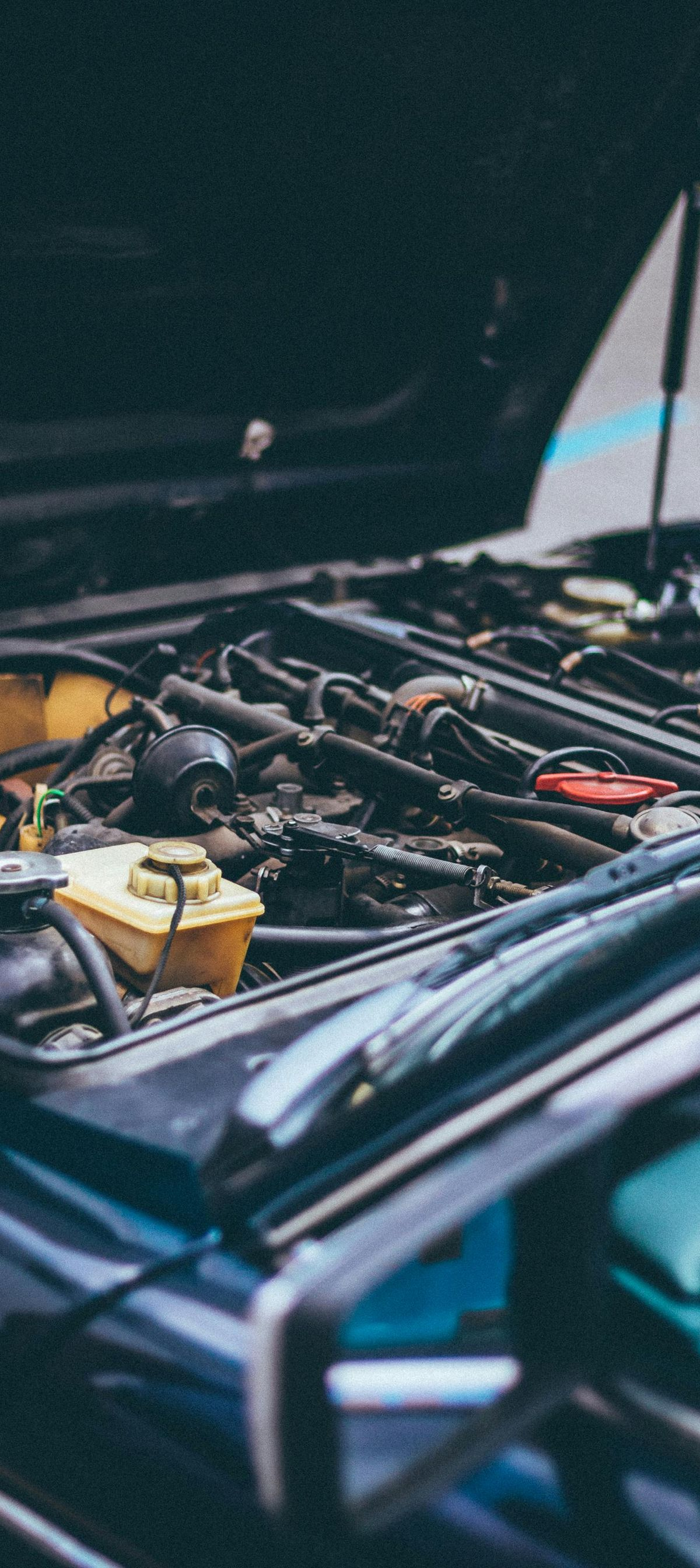 Car engine with hood open, showing a complex network of parts in shades of black and yellow.