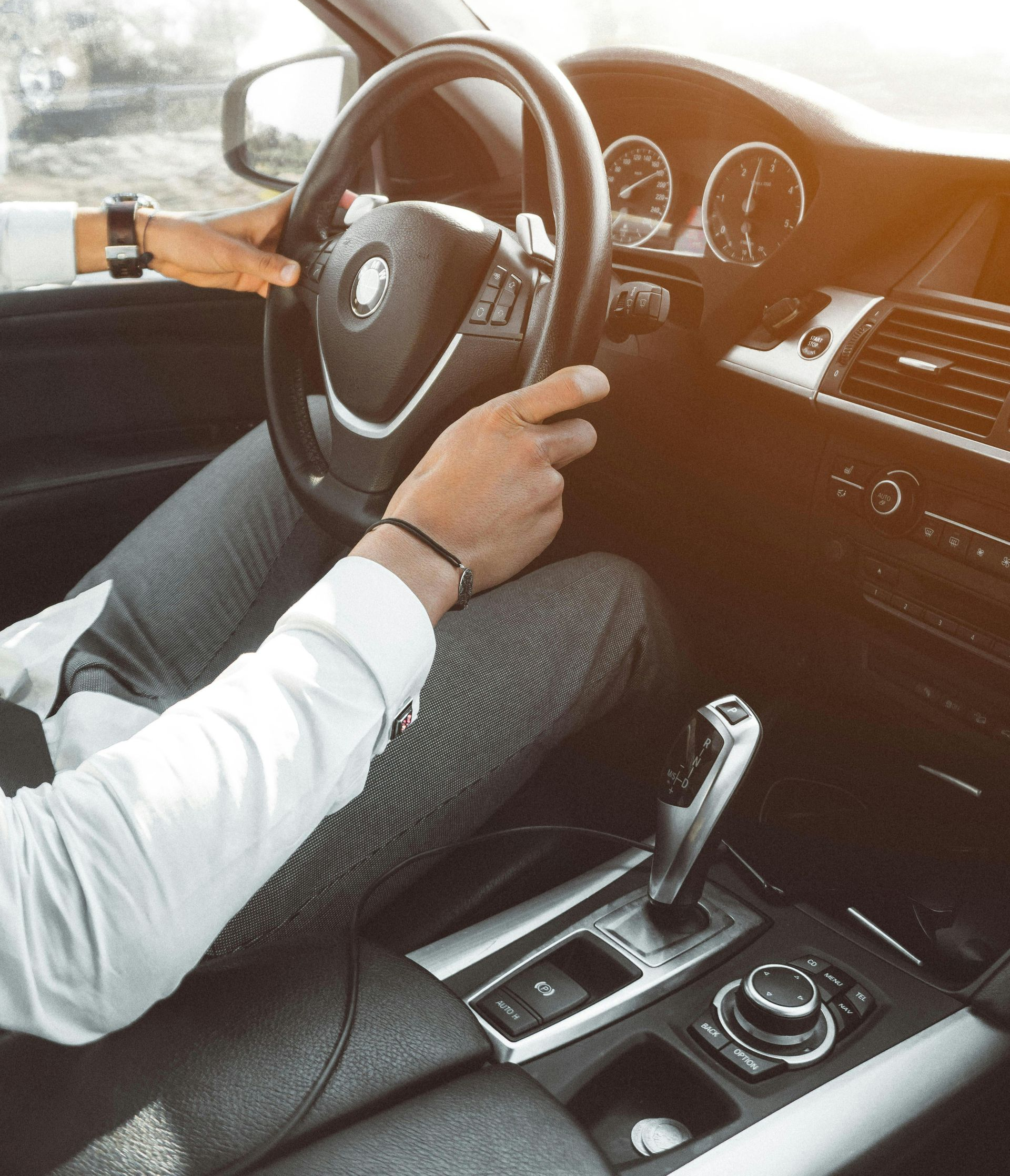 Person driving a car, hands on steering wheel. Interior shot, gear shift visible.