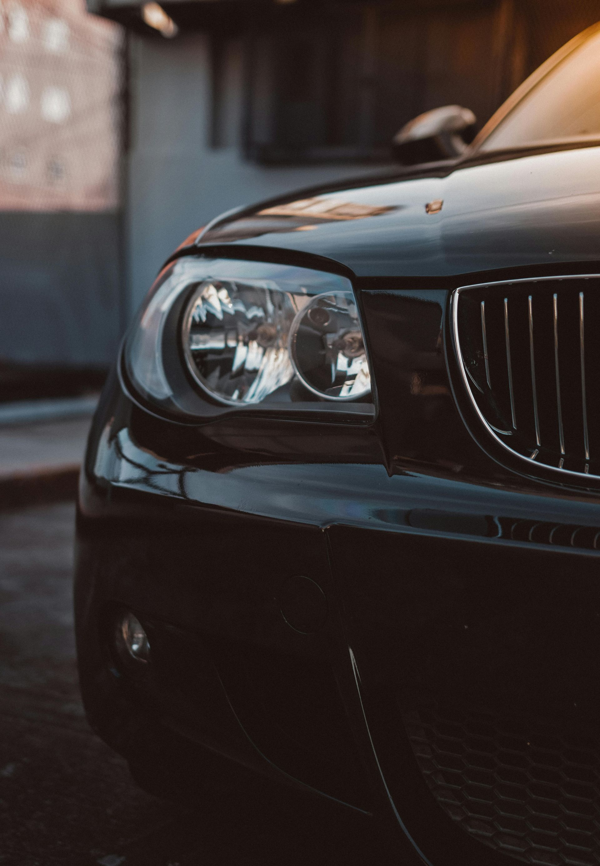 Black BMW car's front with headlight and grill visible; sunlight reflects on the bodywork.