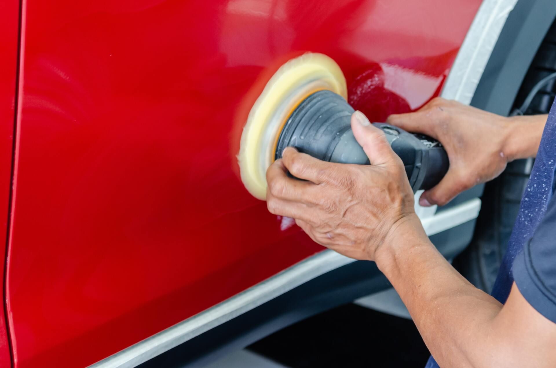 Person using a power polisher to buff a red car door. The tool has a white buffing pad.