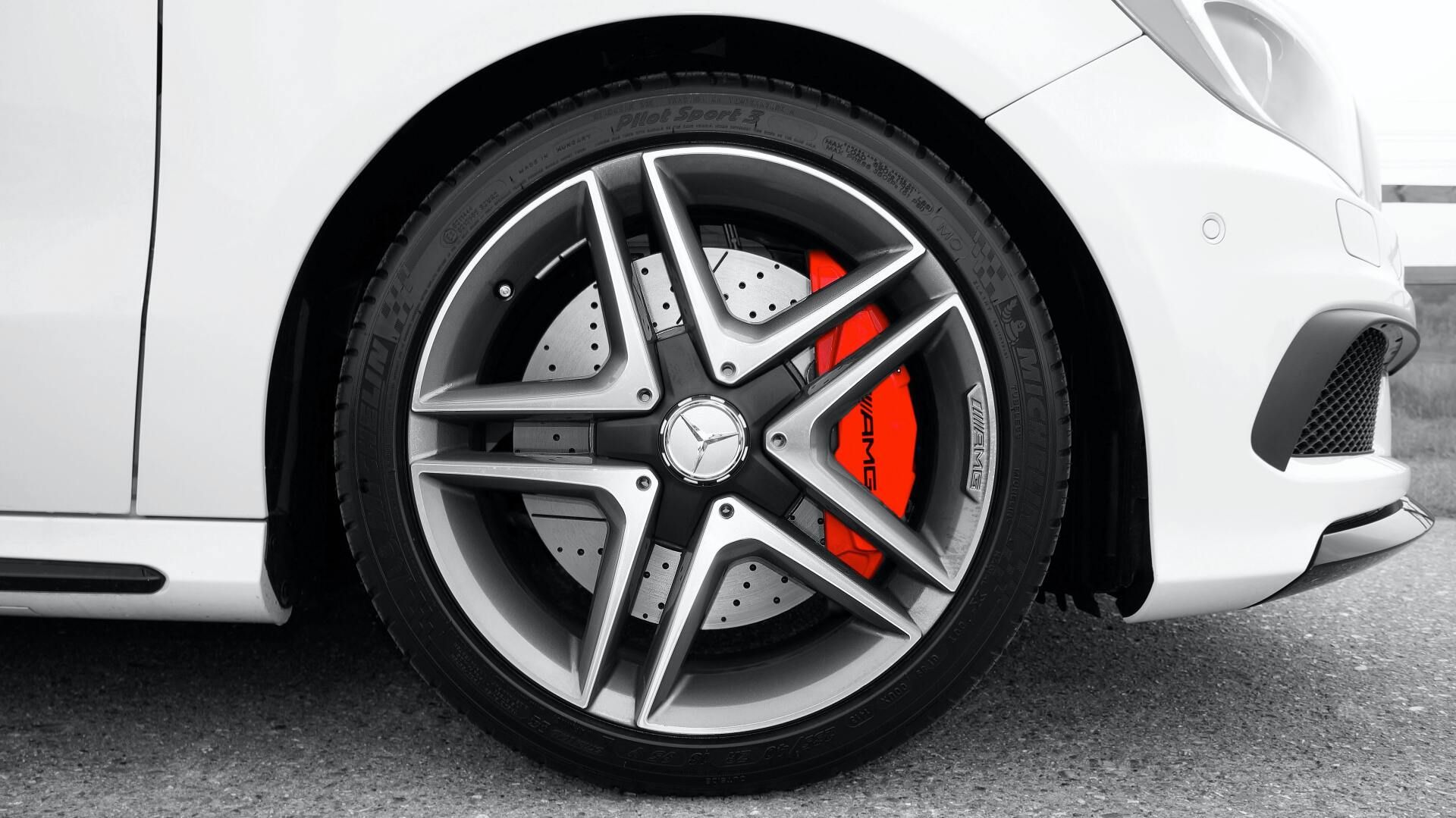 Close-up of a white car's front wheel. The wheel has a silver and black spoke design with red brake calipers.