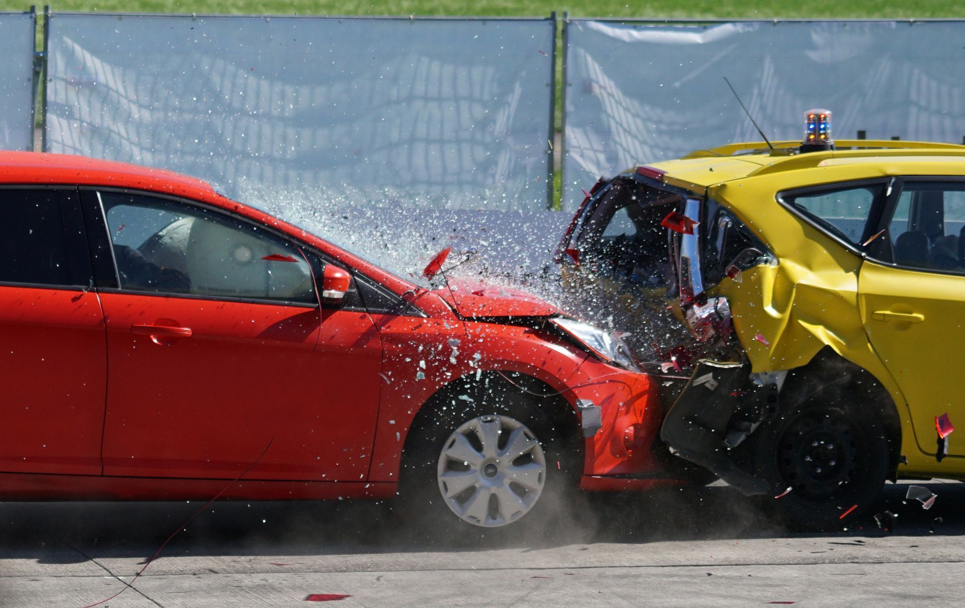 Red car colliding head-on with yellow car, water splashing, damage visible on both vehicles; crash test.