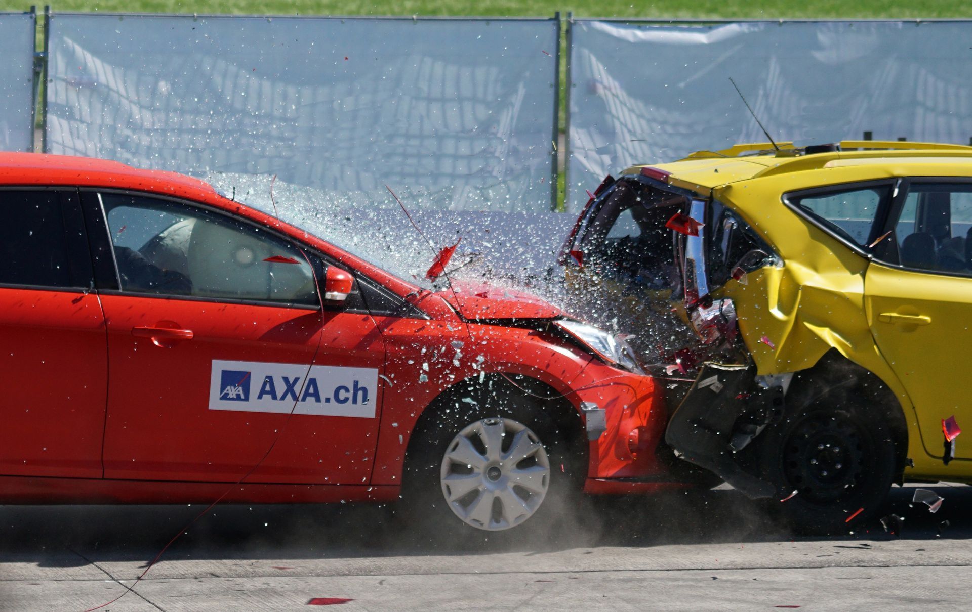 Red car and yellow car in a head-on collision, water spraying. Accident taking place outdoors.