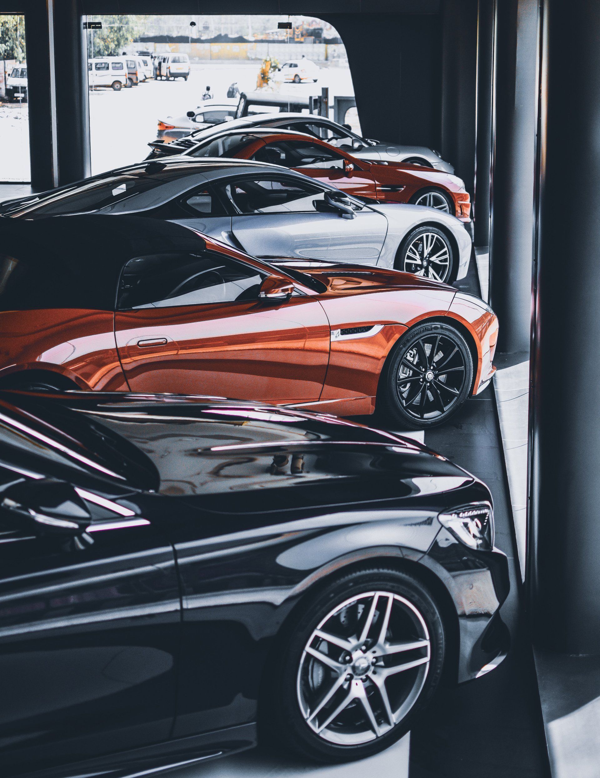 Row of luxury cars in various colors parked indoors, including black, orange, and silver.