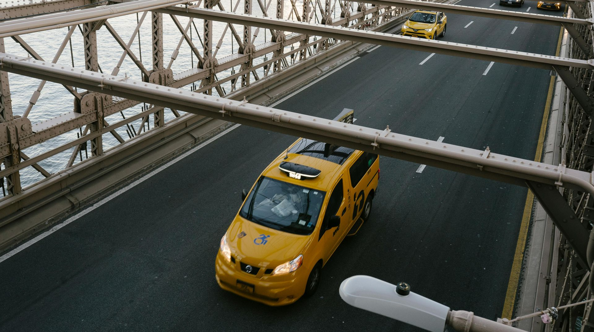 Yellow taxi cabs driving on a bridge, under metal beams.