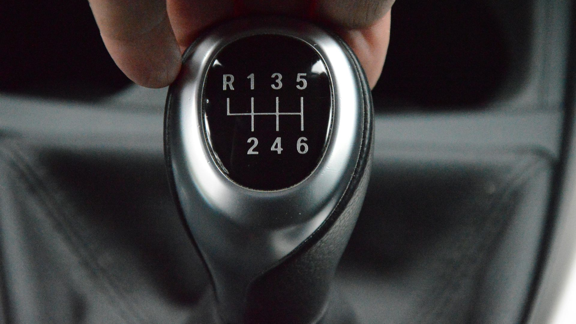 Hand shifting a car's gear stick, showing the 6-speed gear pattern, including reverse.