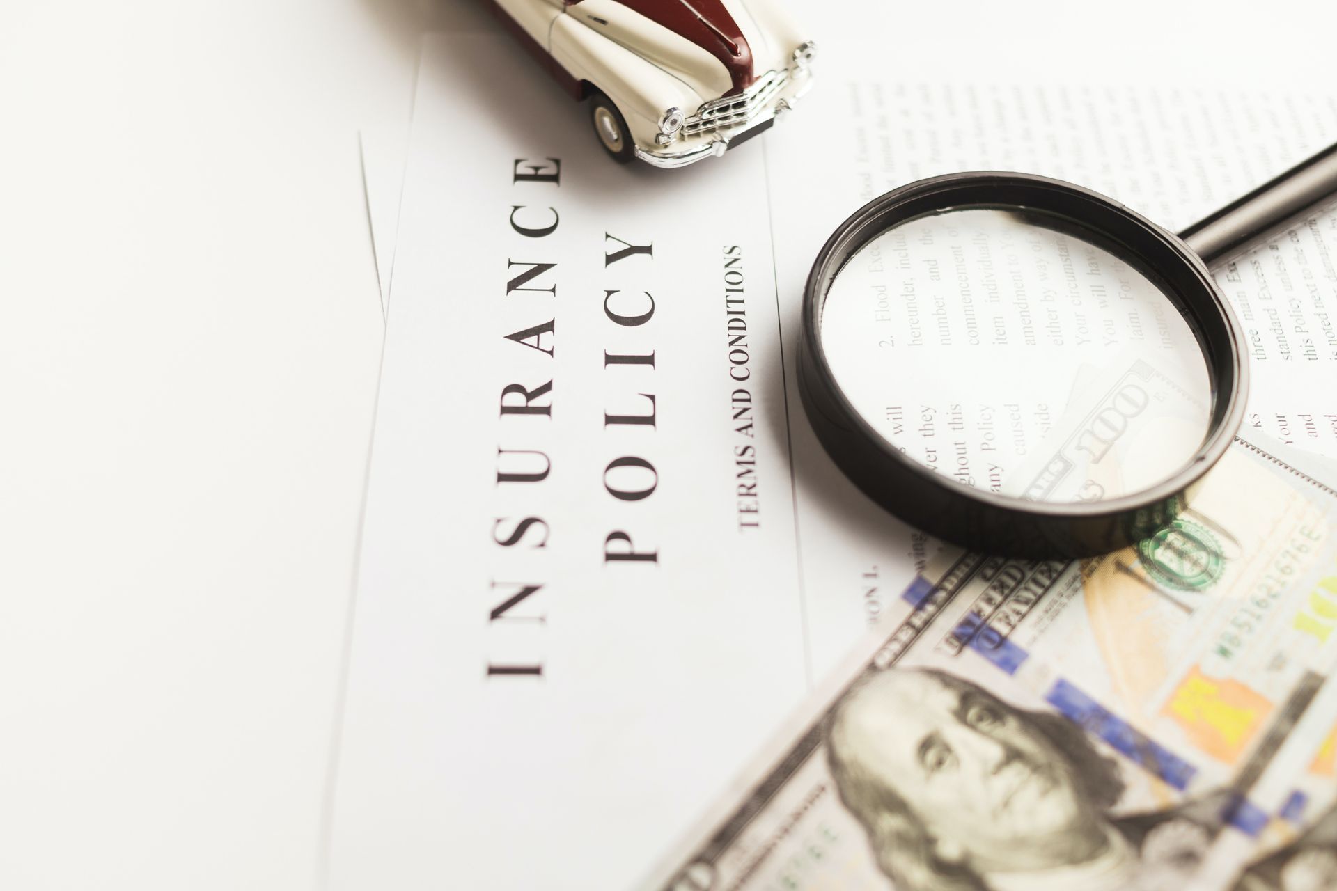 Insurance policy document with a toy car, magnifying glass, and cash.