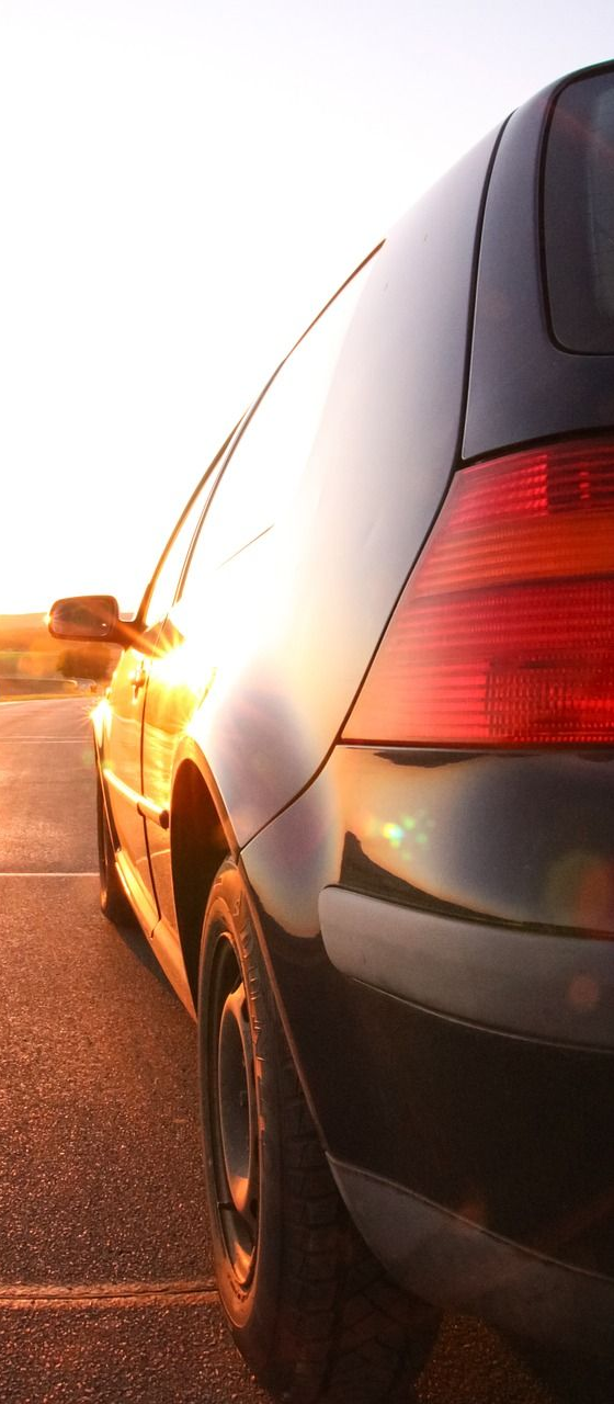 Black car parked on a road with the sun setting in the background.