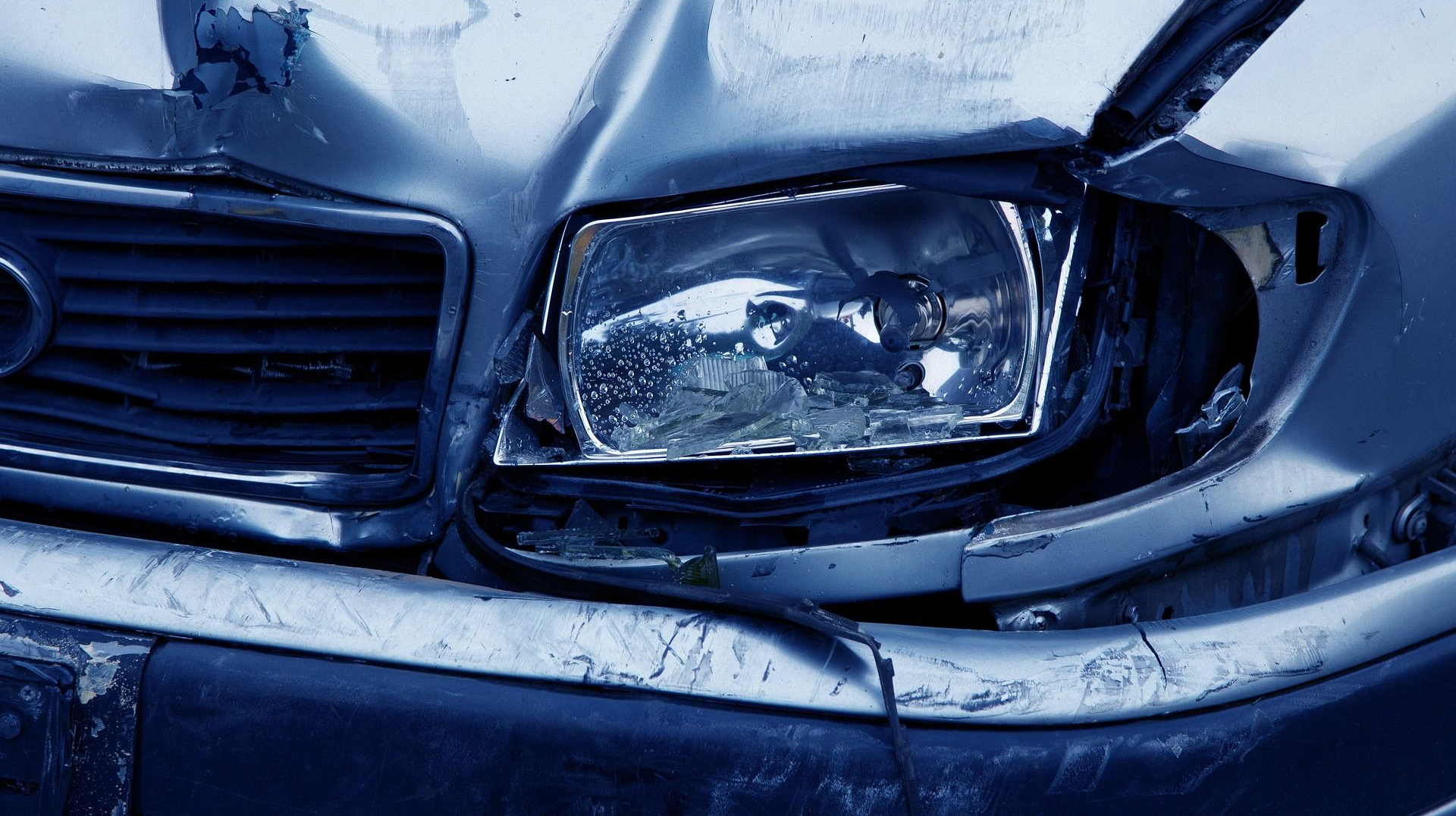 Damaged silver car headlight and hood after a collision.