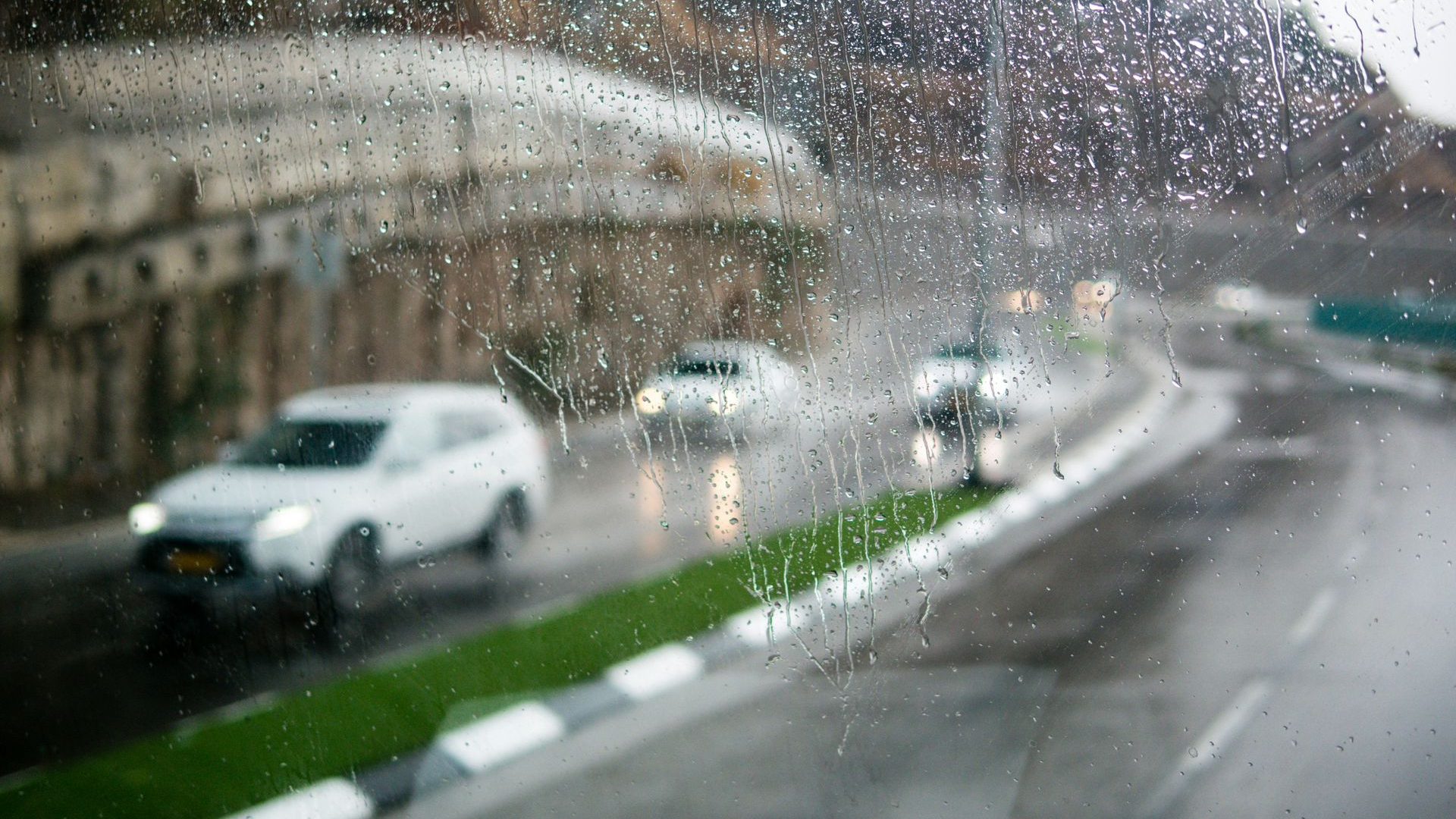 Rainy view through a window of cars driving on a wet road, alongside a tunnel and a green patch.