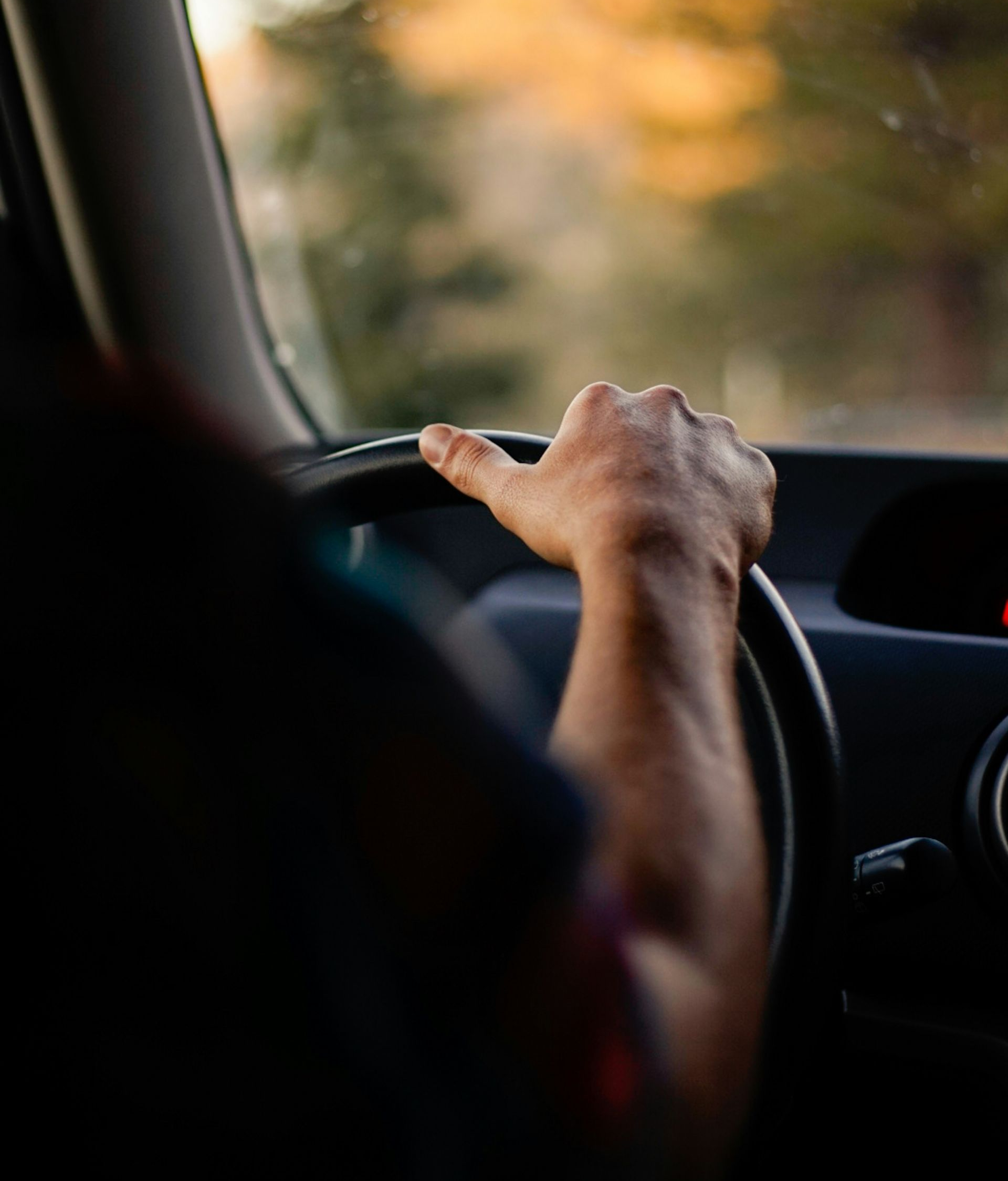 Hand gripping a car steering wheel; person driving.