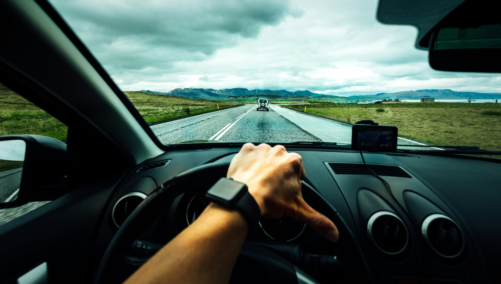 Hand on steering wheel, driving on a road under a cloudy sky.