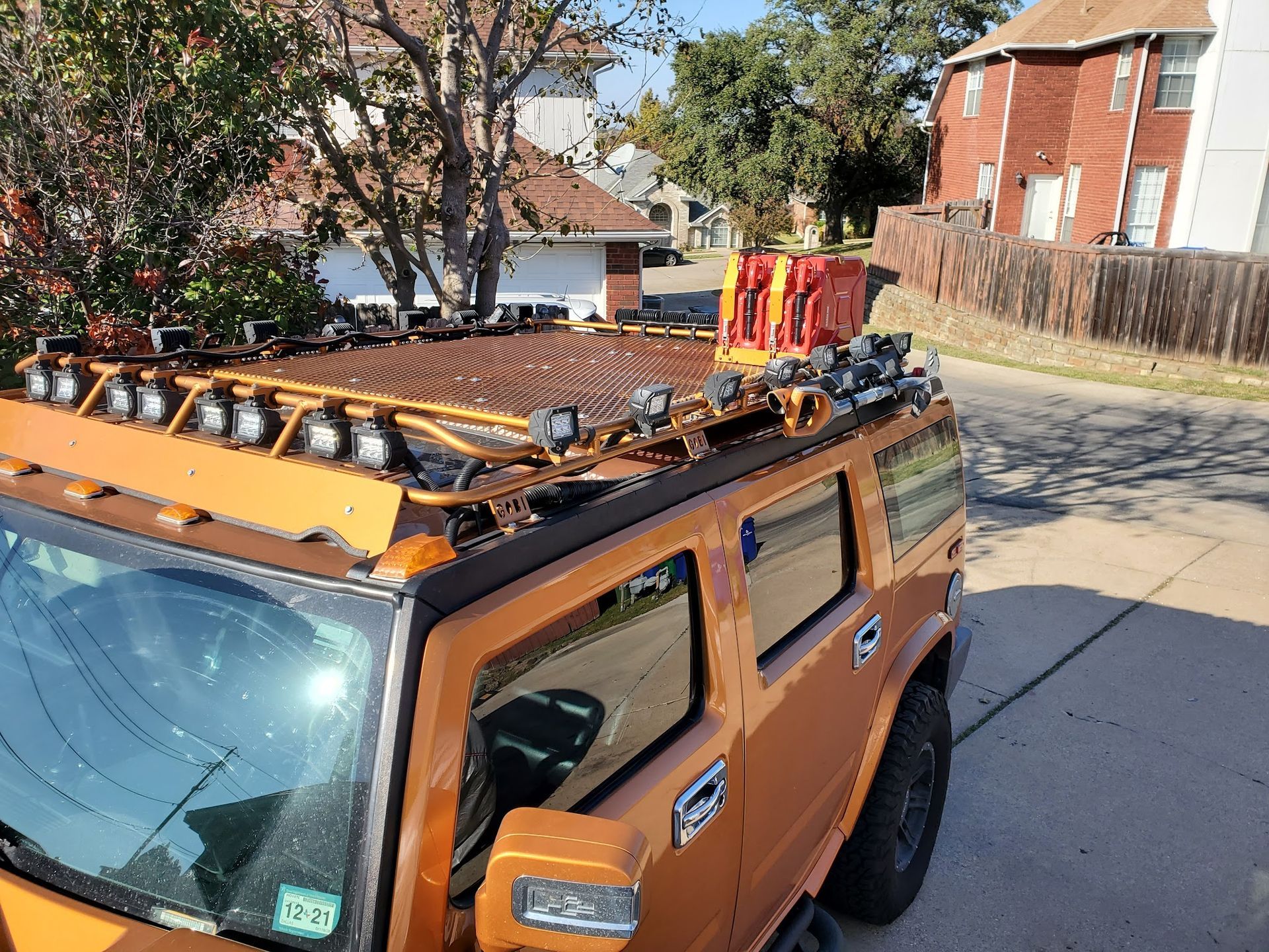 Orange Hummer with a custom roof rack, covered in lights and a gas can, parked on a street.