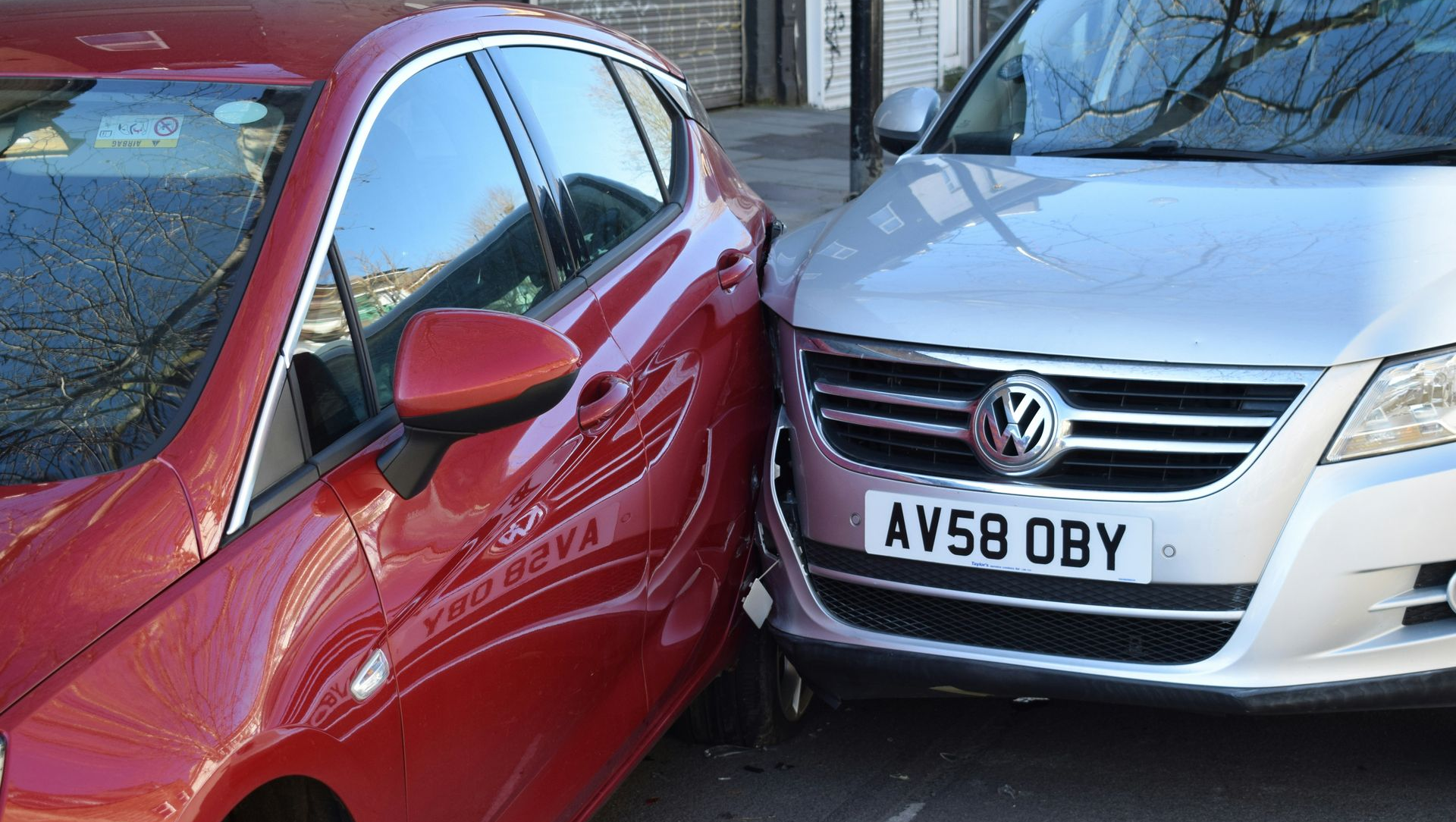 A silver Volkswagen has crashed into the side of a red car on a city street.