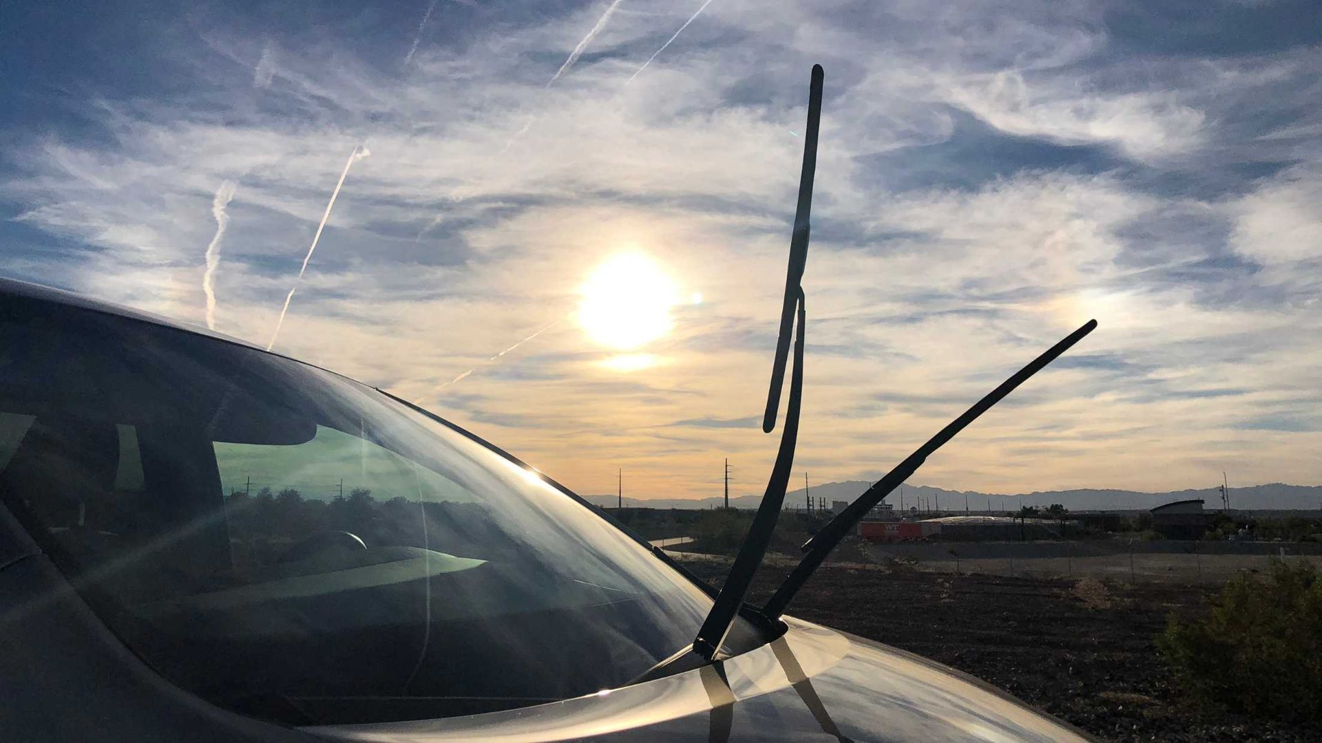 Car windshield with wipers up against a bright, sunny sky.