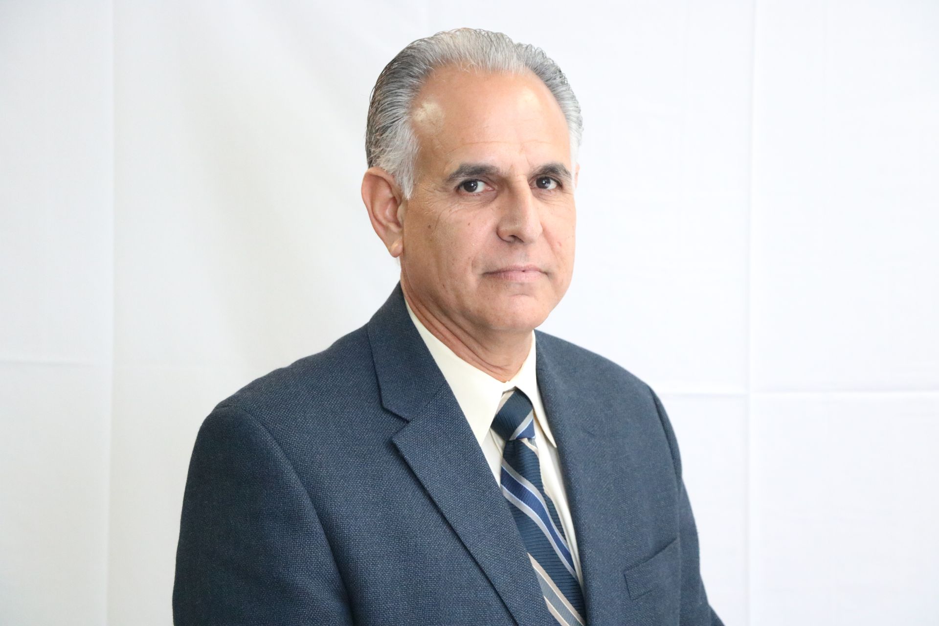 Man in a blue suit, light shirt, and tie against a white background; looking at the camera.
