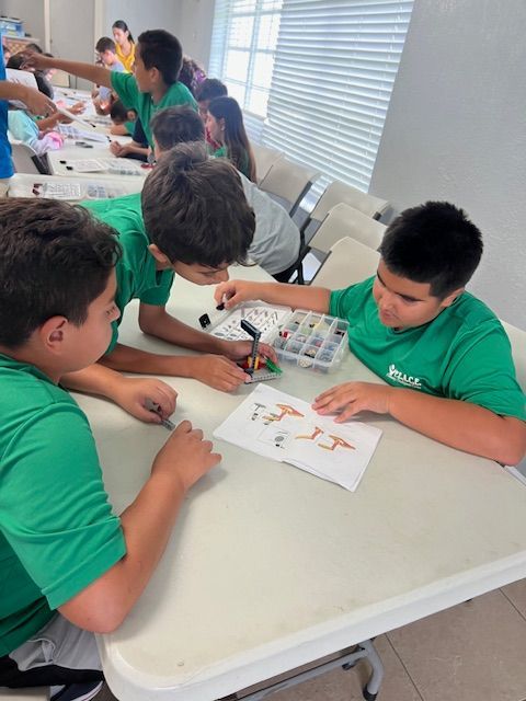 Children in green shirts building with Lego bricks at a table.