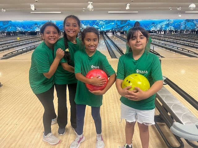 Four girls in green shirts pose at a bowling alley, holding bowling balls.
