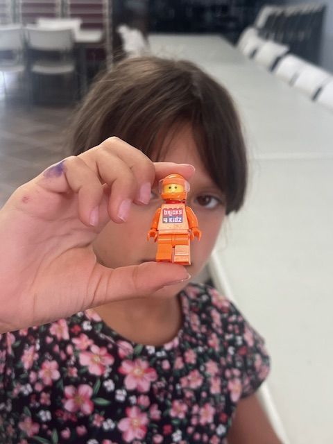 Girl holding up an orange Lego mini-figure in front of her.