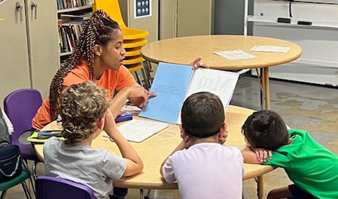 Woman reading a book with three children at a round table.