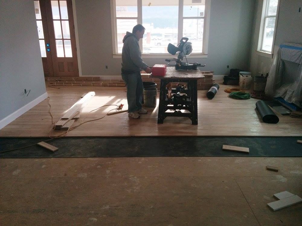 A man is working on a wooden floor in a living room.