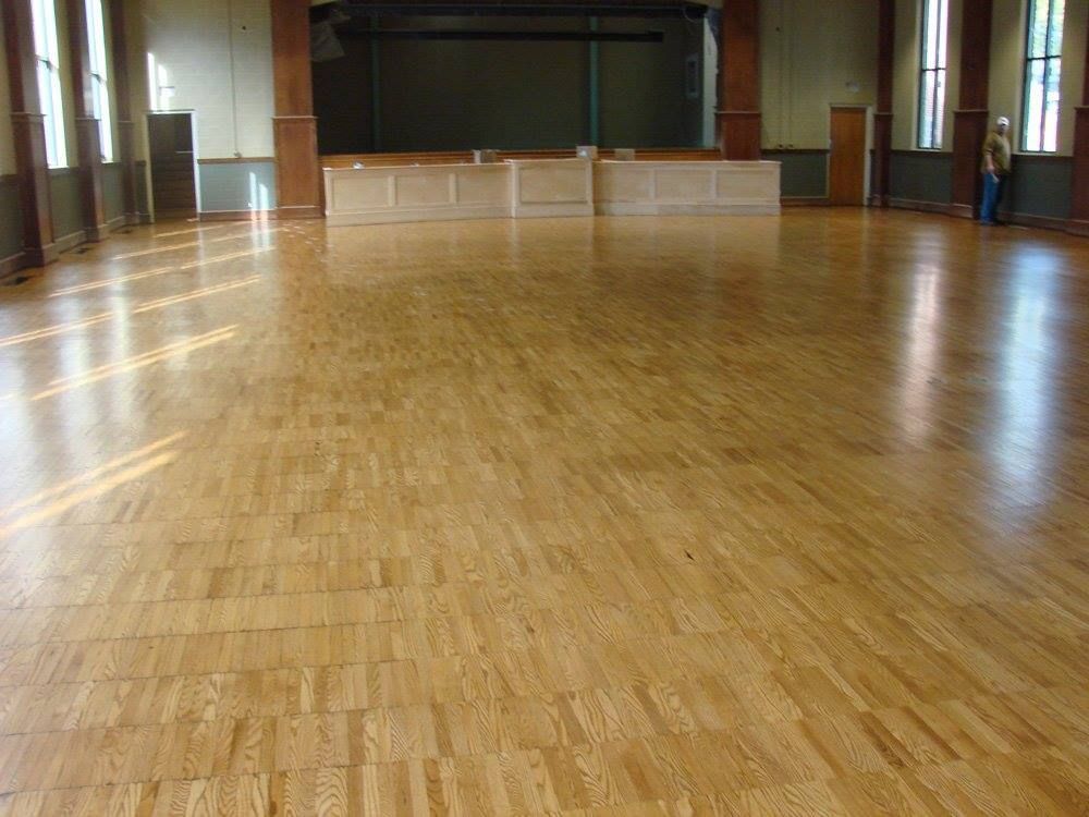 A large empty room with a wooden floor and a stage in the background.