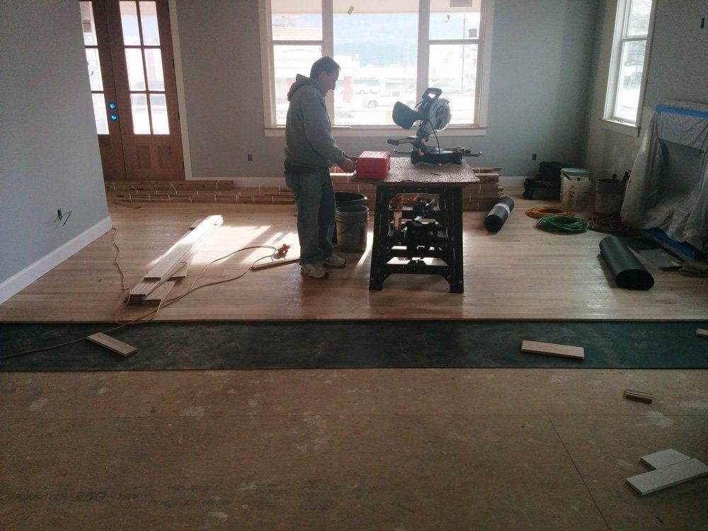 A man is working on a wooden floor in a living room.