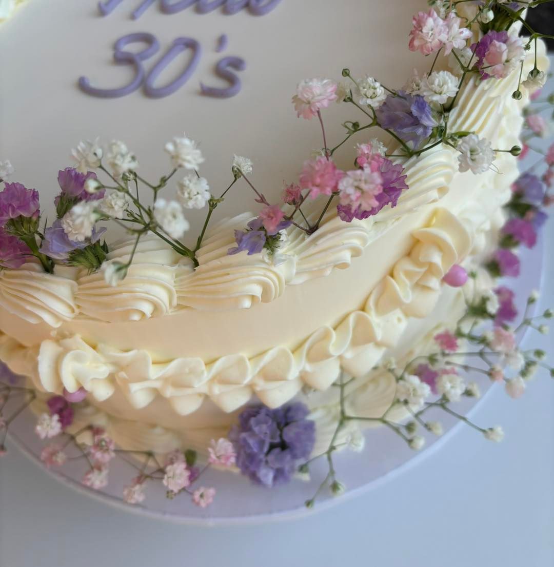 Torta decorata con glassa alla crema, fiori freschi e la scritta 