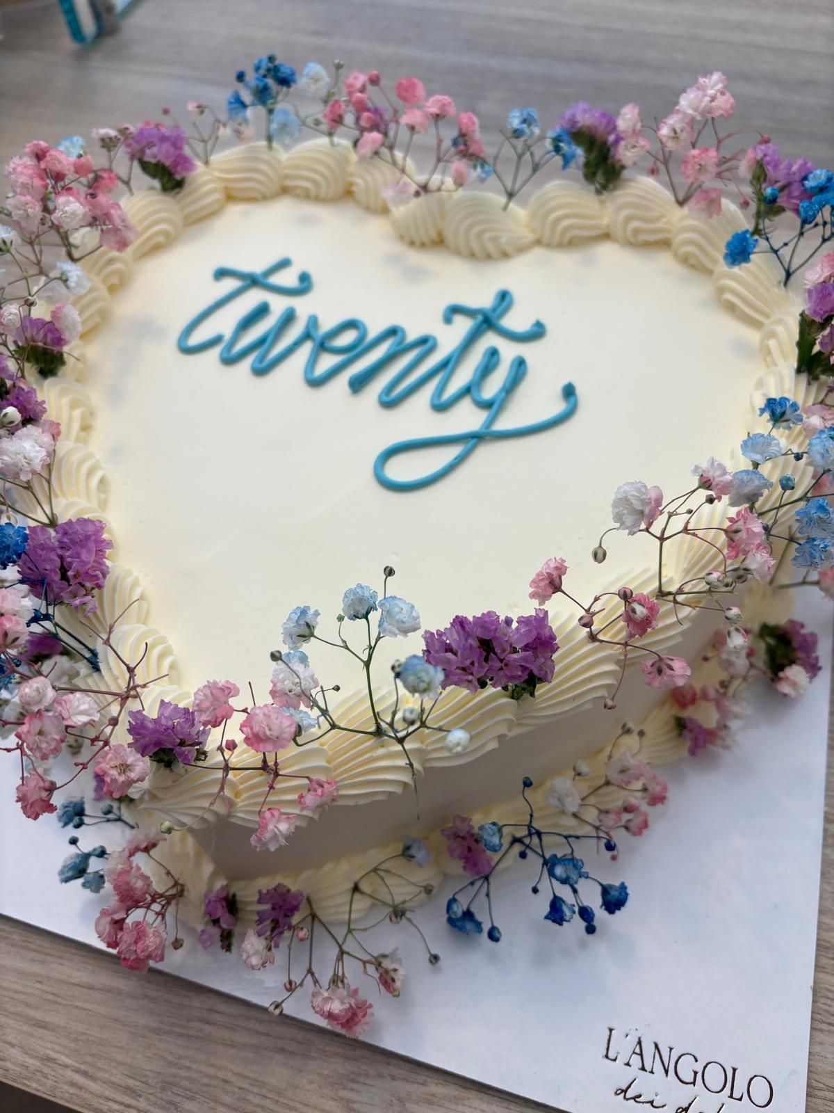 Due dessert a forma di cuore con strati di cioccolato e glassa bianca, guarniti con lamponi, su piatti da portata neri.