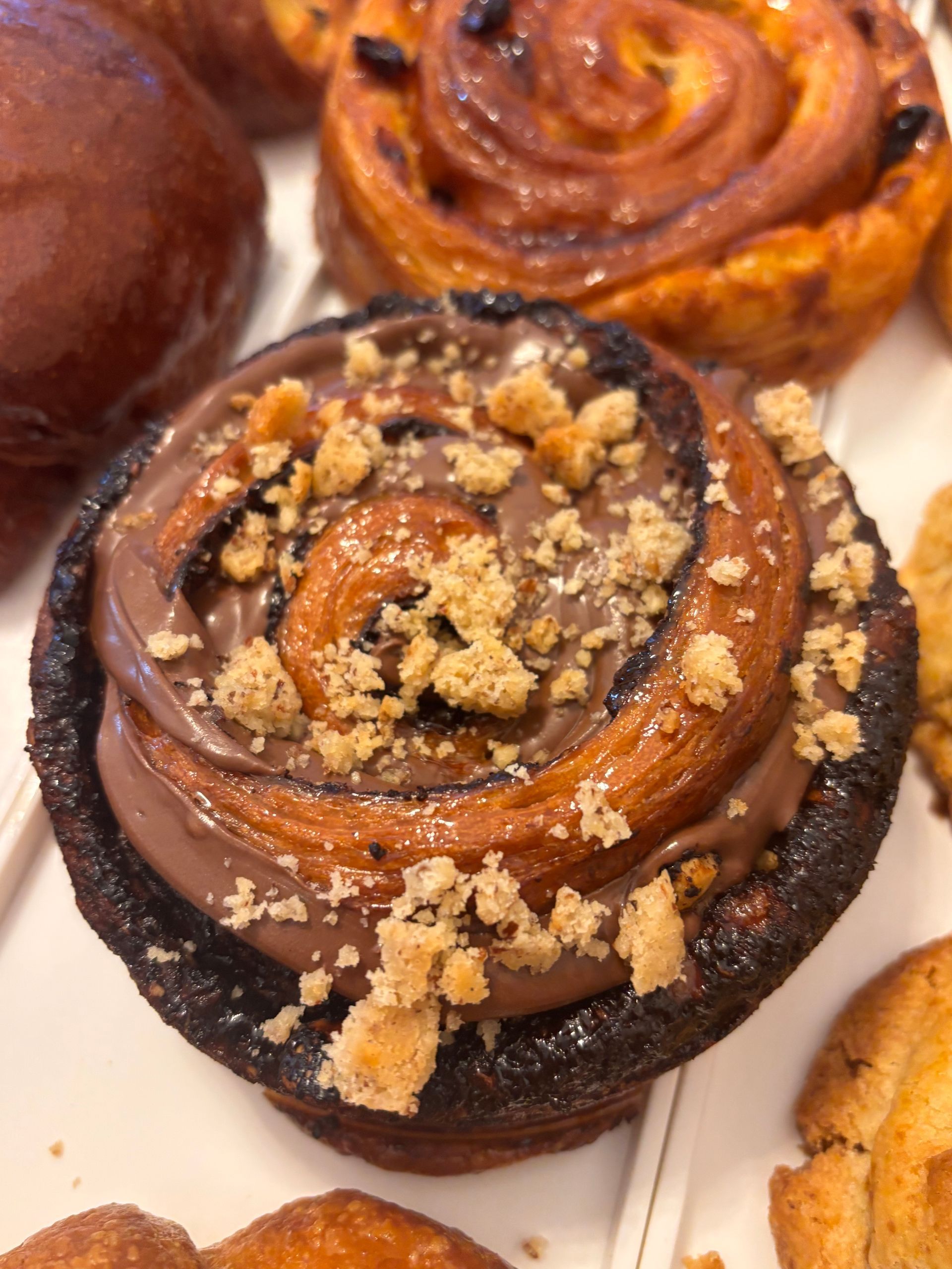 Un cucchiaio di burro di nocciole gocciola in un bicchiere. Su un tagliere di legno ci sono pane, noci e una caffettiera.