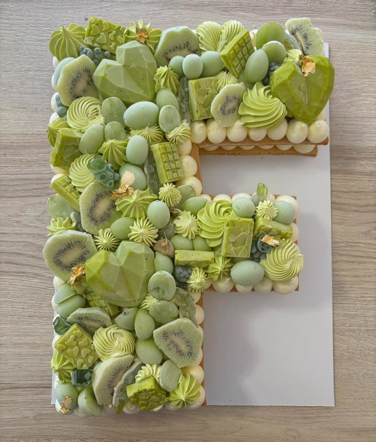 Torta a forma di cuore decorata con glassa bianca, cioccolato, fragole e macaron su una superficie scura.