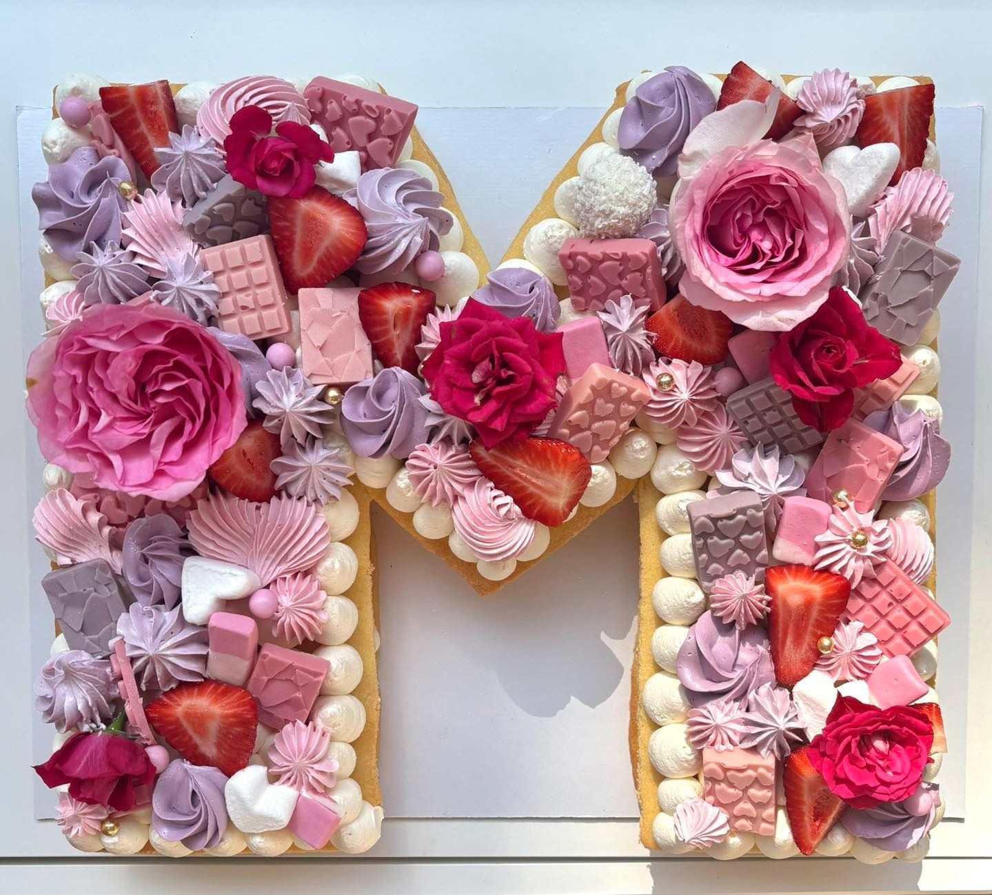 Primo piano di una torta al cioccolato decorata con frutta fresca, meringhe e un vortice arcobaleno, su un piatto d'oro.