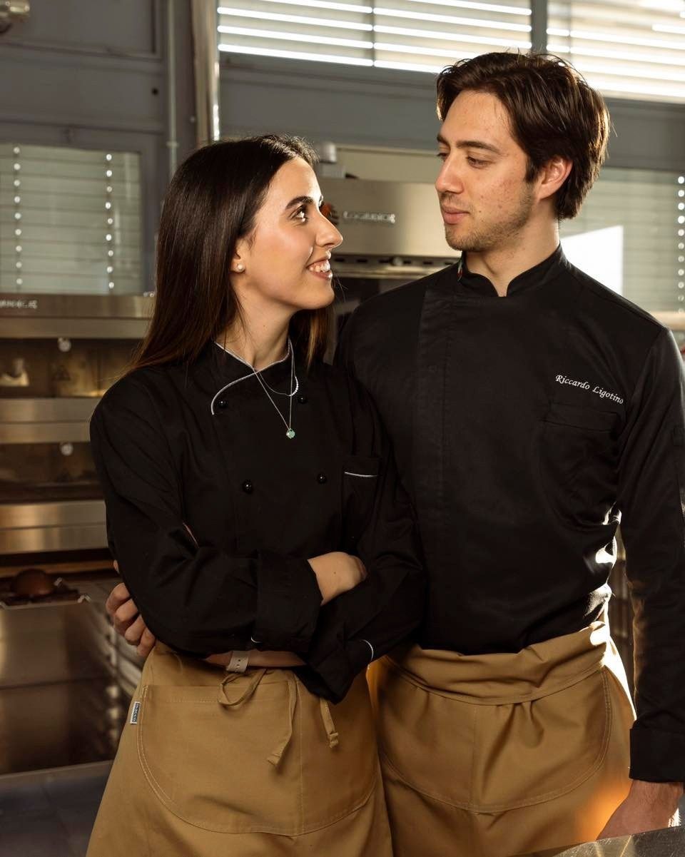 Cuochi, uomini e donne, in giacca e grembiule neri, si guardano in cucina.