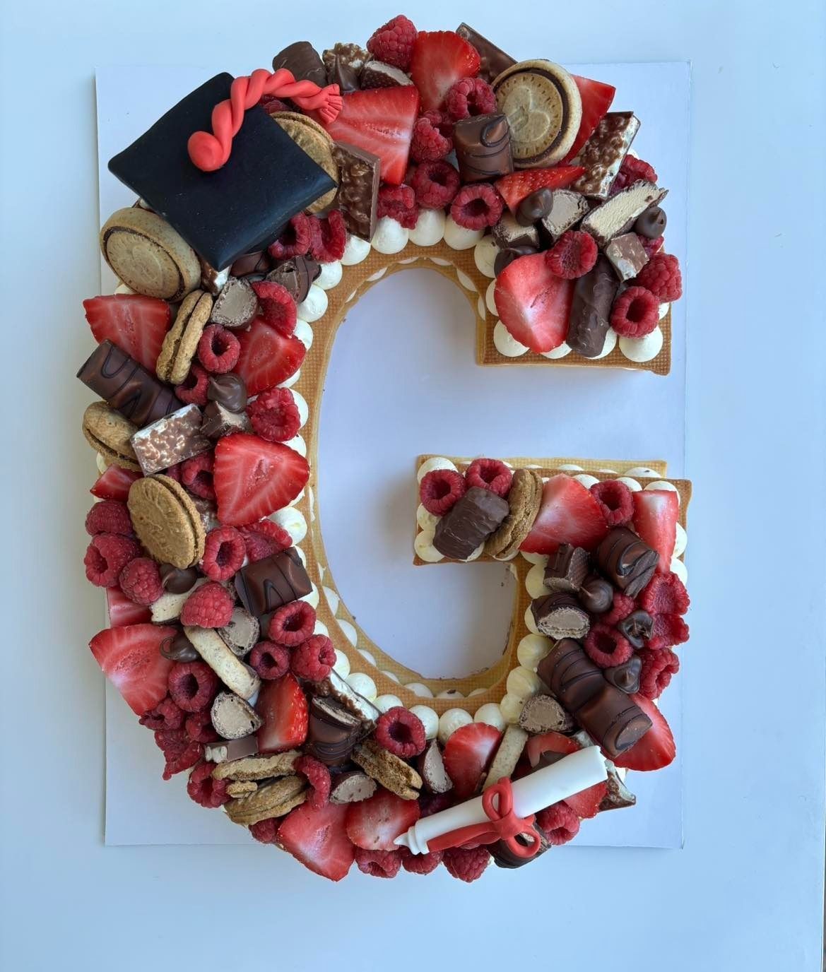 Torta di laurea con la lettera "G" e frutta e cioccolato.
