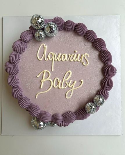 Torta alla lavanda con la scritta "Aquarius Baby" in bianco e dettagli a forma di palla da discoteca.