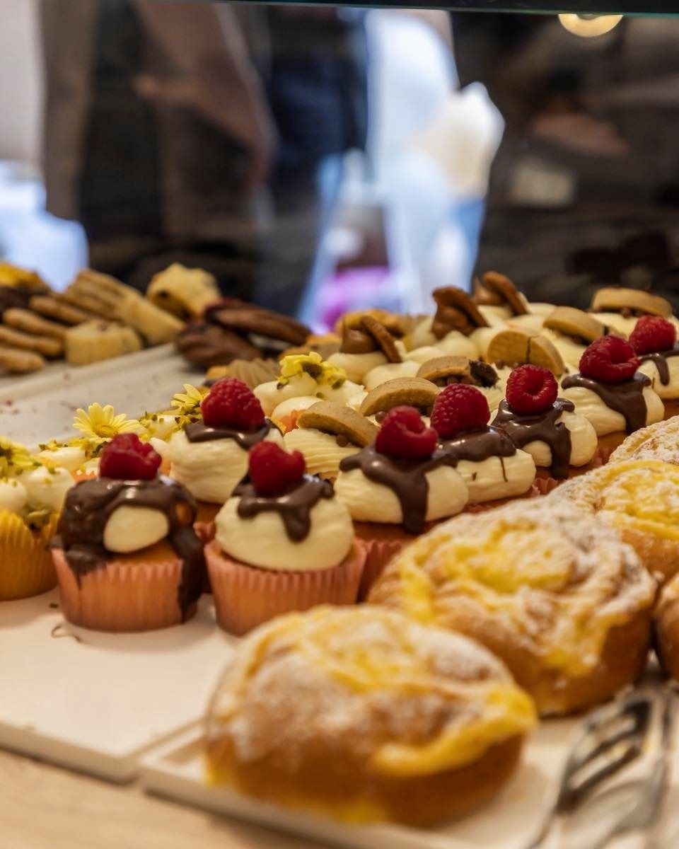 Caffè in una tazza decorata, limone, dolce e cucchiaino disposti su una tavola di legno.