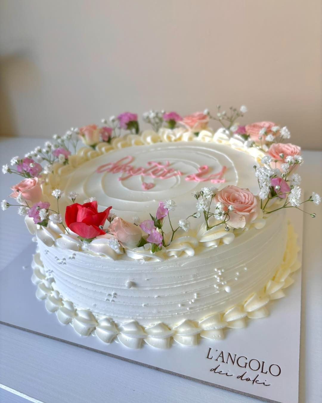 Torta decorata con fiori e glassa rosa con la scritta 