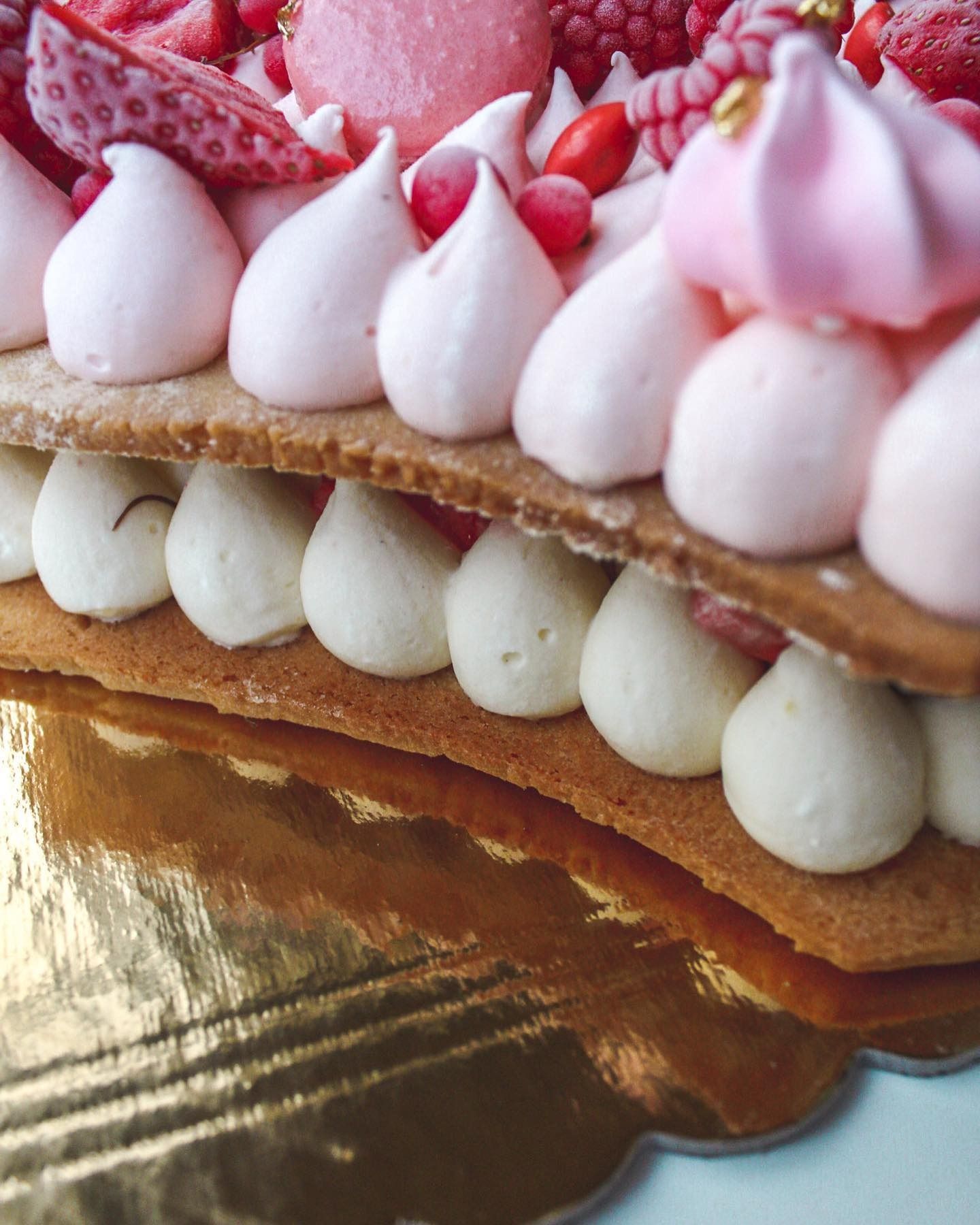 Dessert di pasta sfoglia a strati con glassa rosa e bianca, frutti di bosco e base in lamina d'oro.