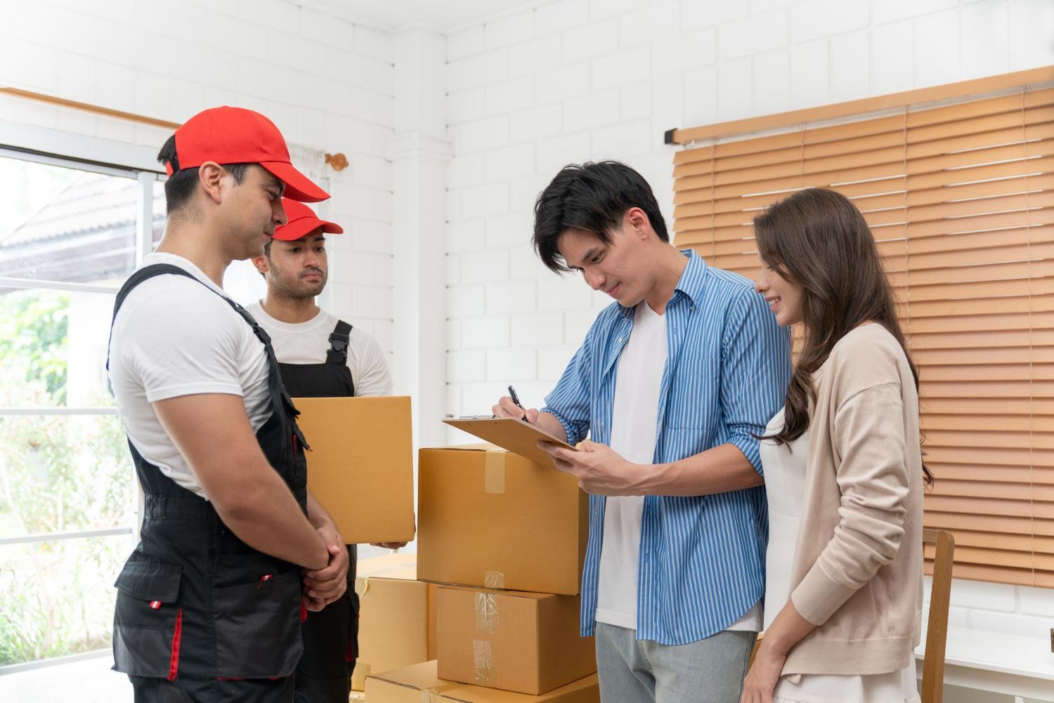 A group of people are standing in a room with boxes and a man is writing on a clipboard.