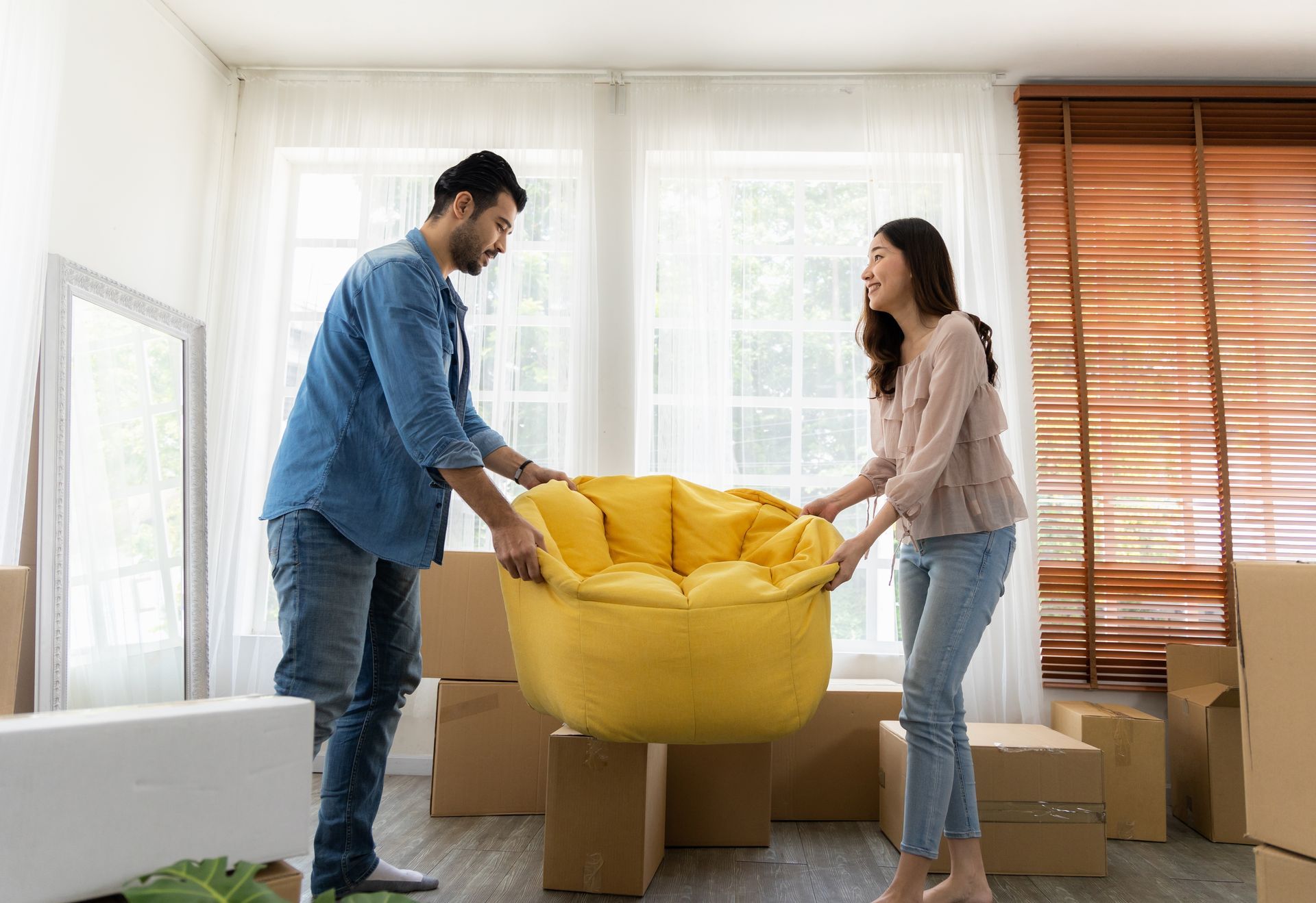 Couple moving yellow beanbag chair in a bright room with boxes.