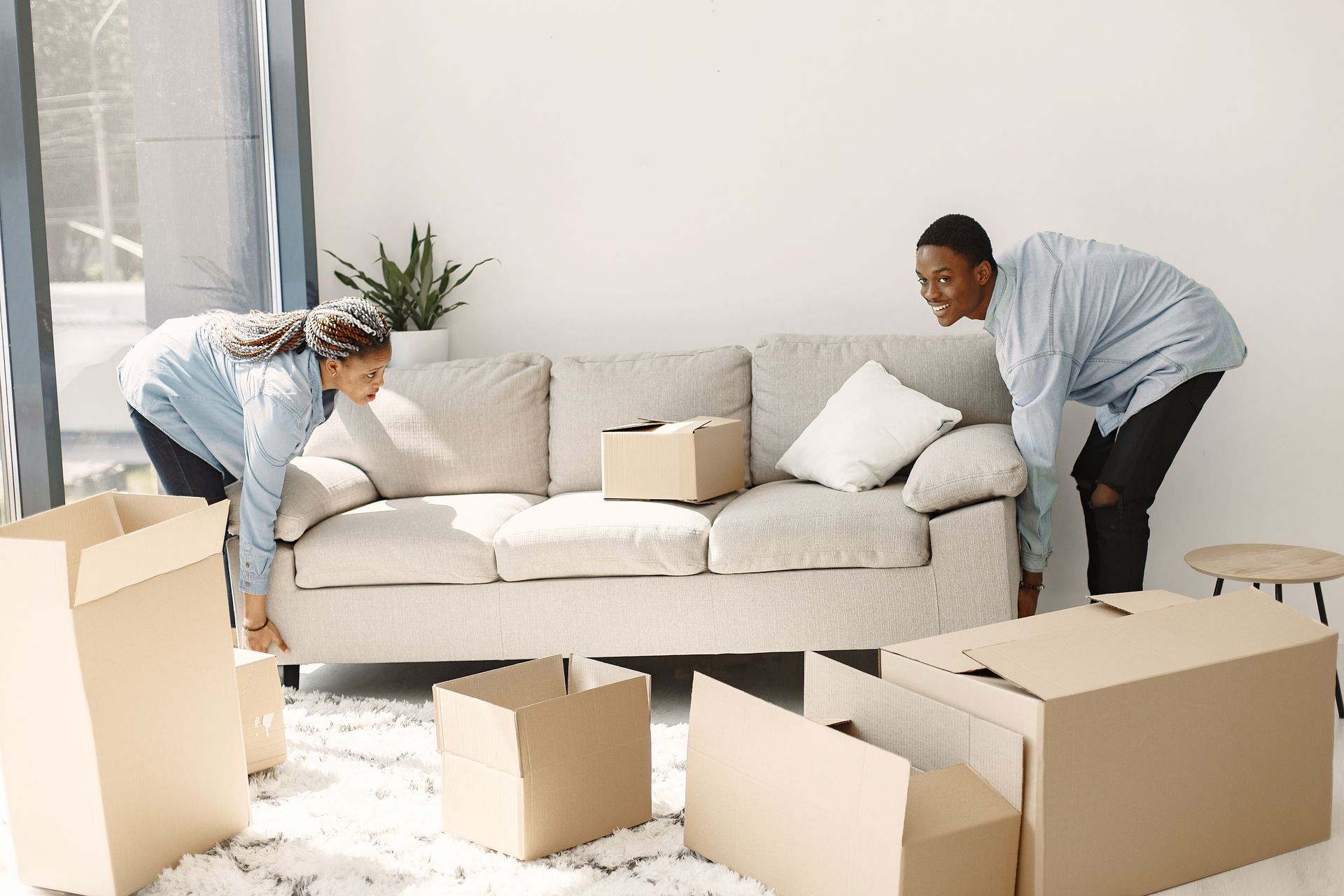 Two people lifting a couch, surrounded by moving boxes, indoors.