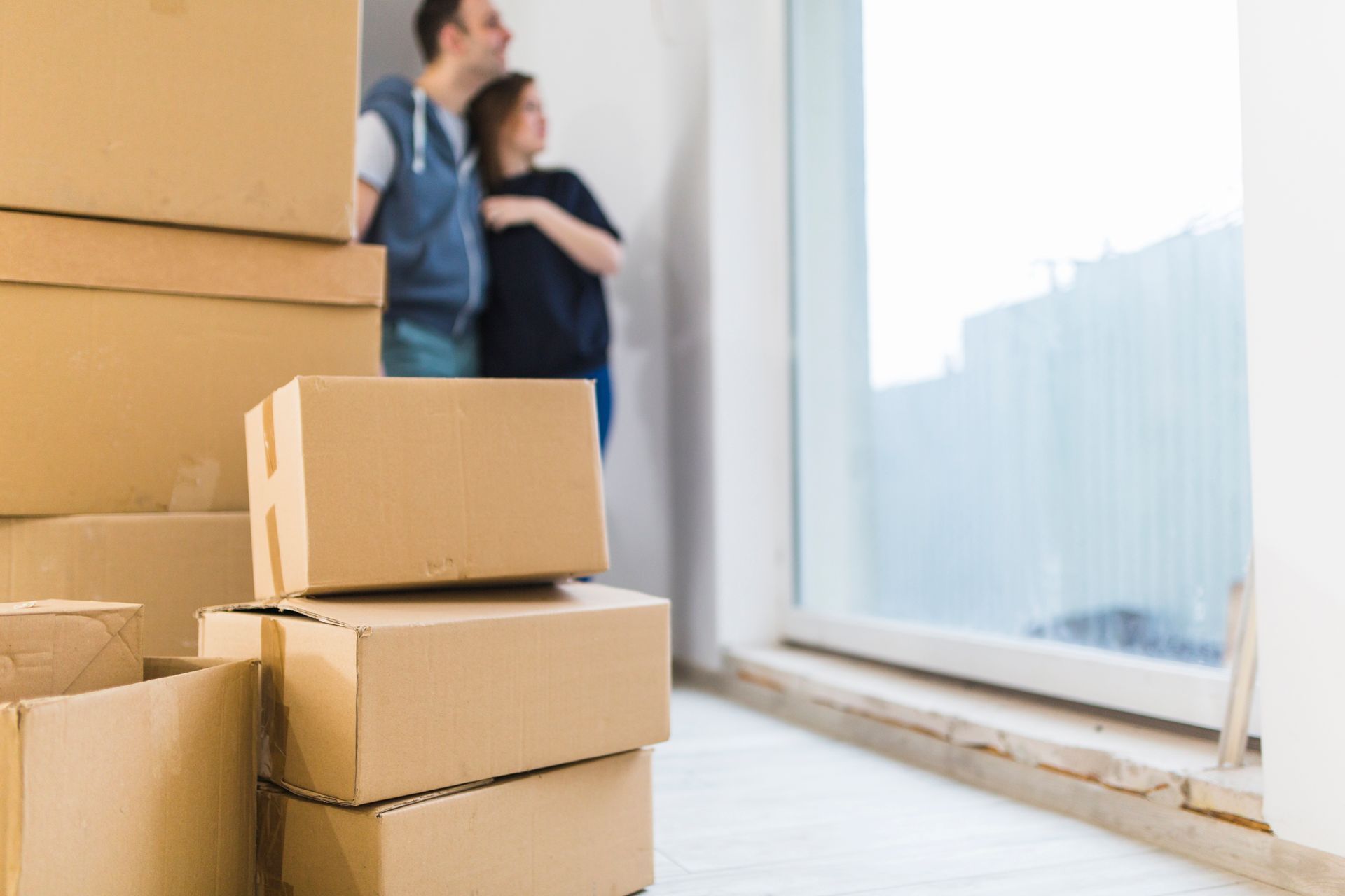 A man and a woman are standing in a room with boxes stacked on top of each other.