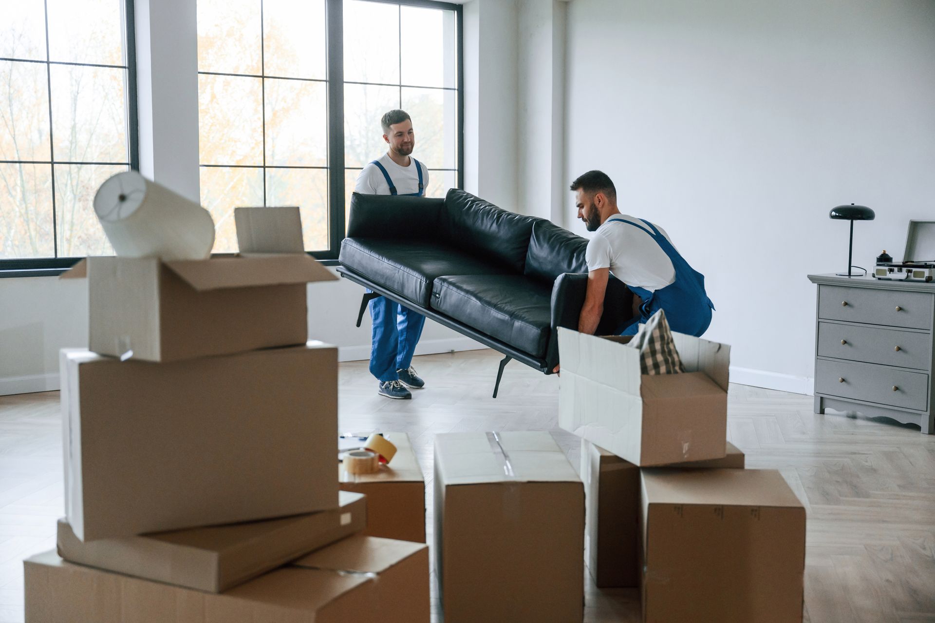 Two men are carrying a couch in a living room.
