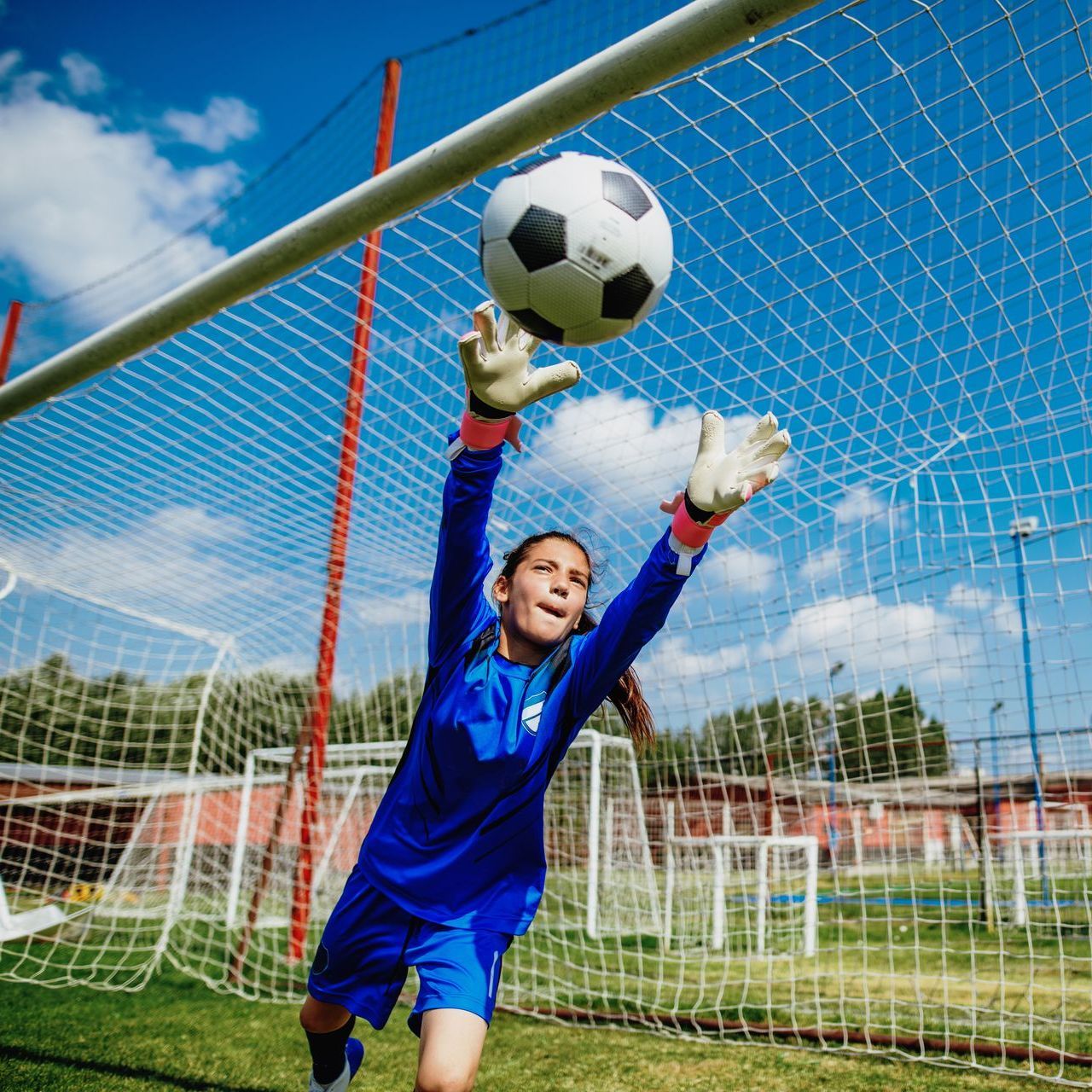 Young girl catching a soccer ball with next in background.
