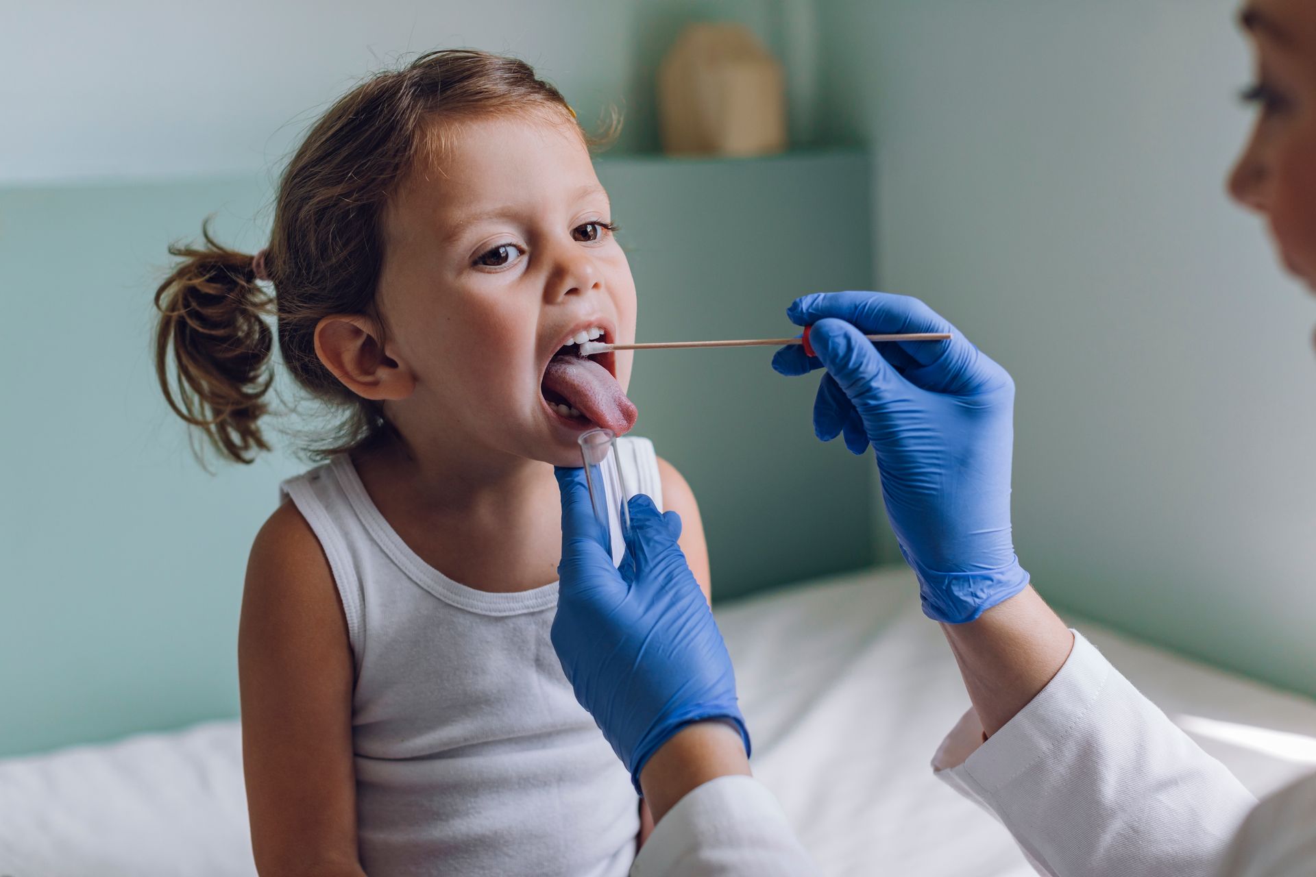 A little girl is getting her throat examined by a doctor.