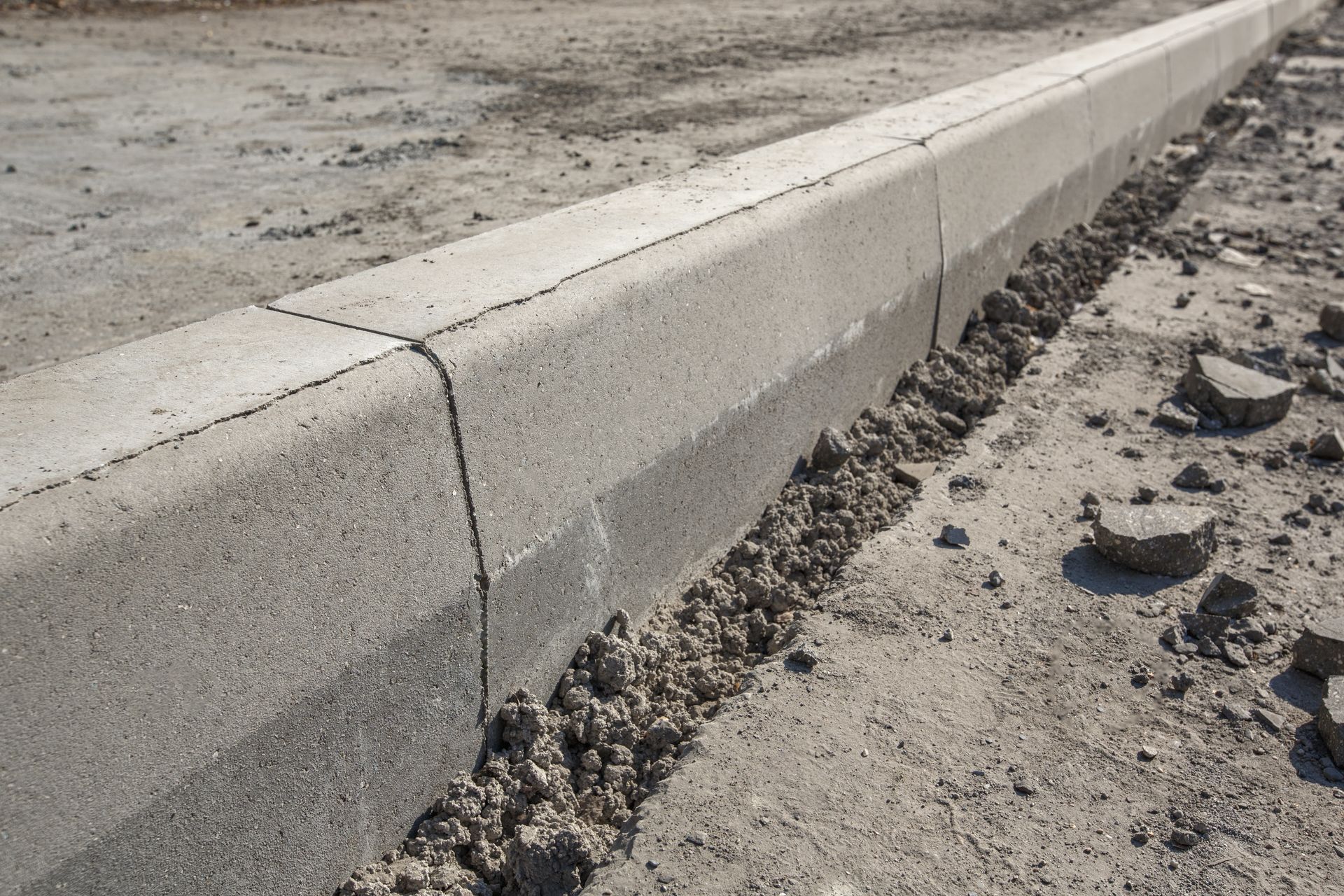 Gray concrete curb segments installed along a dusty, unpaved construction site ground.